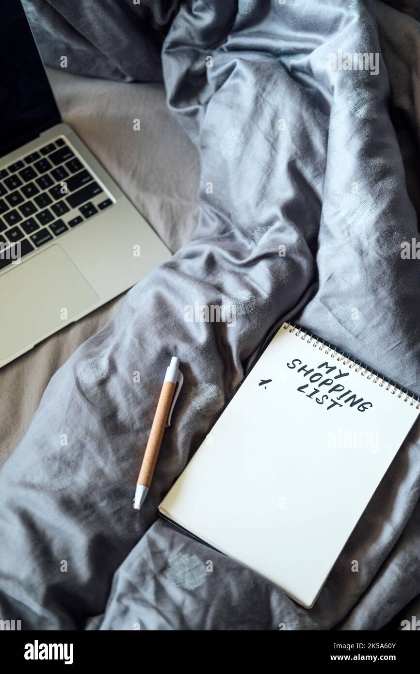 Sparsame Tipps für das Leben, Sparkonzept mit Einkaufsliste im Notebook in der Nähe von Laptop und Tee-Kaffeetasse in Bad zu Hause Stockfoto