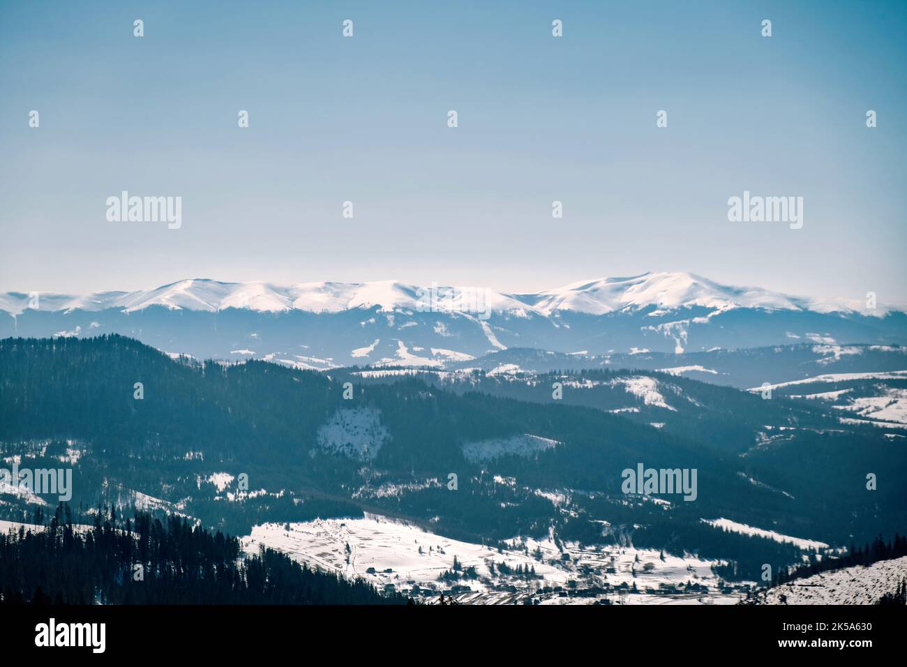 Panoramablick auf die verschneiten Berge. Blick auf Berge mit Wiesen und Hütten mitten im Wald und im Hintergrund Berggipfel Stockfoto