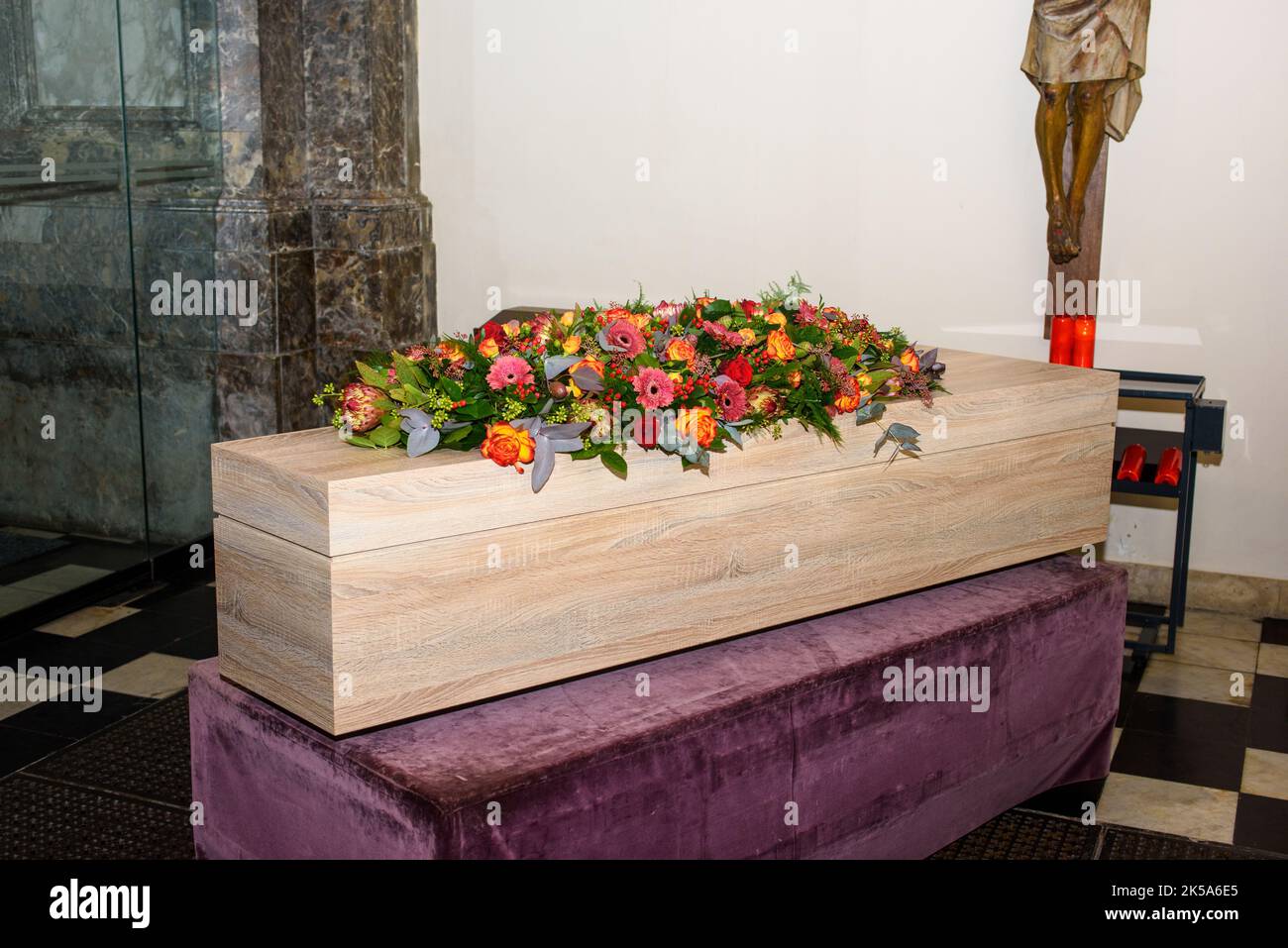 Sarg mit Blumen auf ihm in der Kirche mit Jezus Christus an der Wand warten auf den Transport für den Gottesdienst Stockfoto