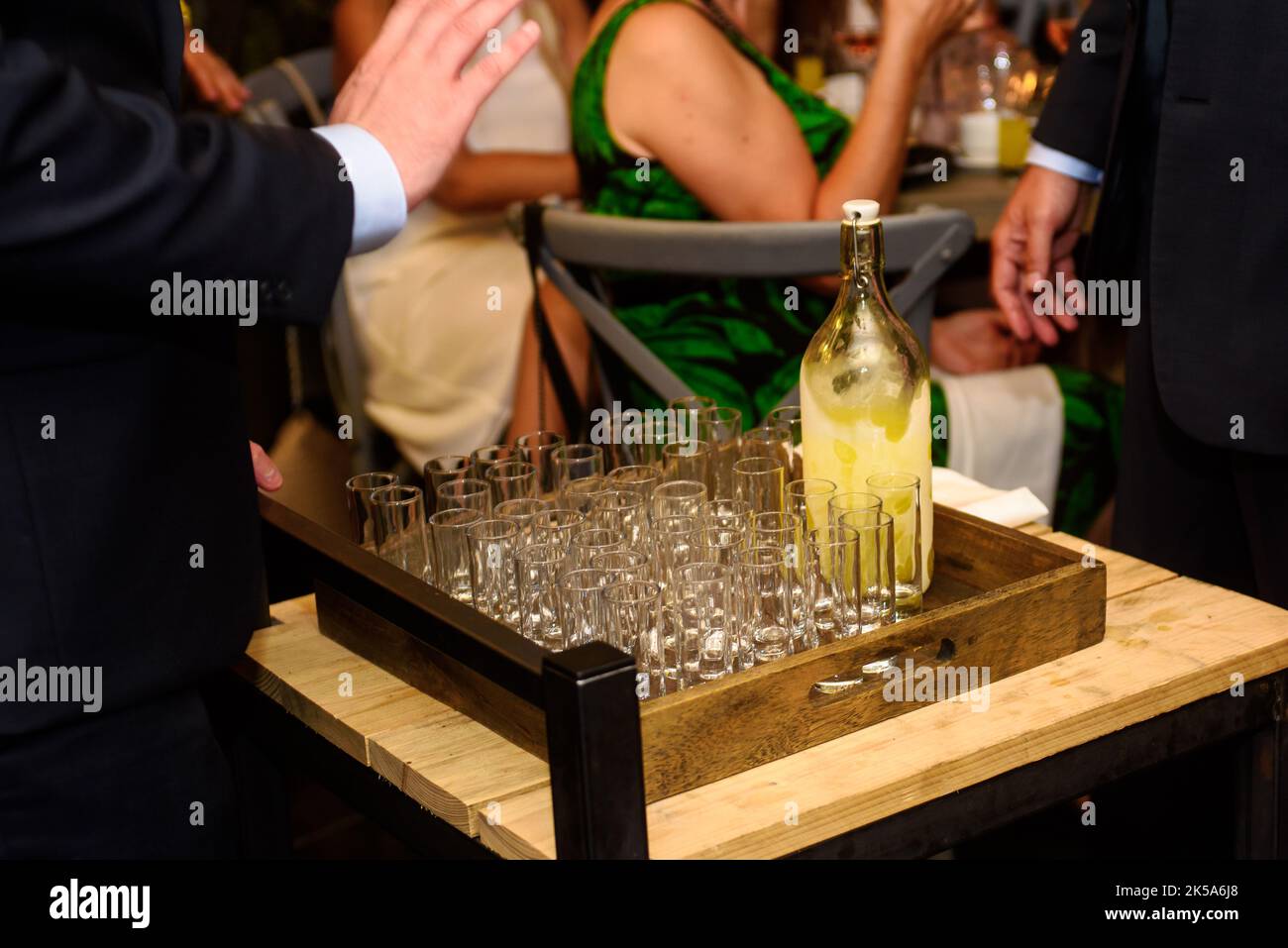 Nahaufnahme eines Kellners, der Limoncello in Gläsern mit einem kleinen Holztisch auf einer Party serviert Stockfoto