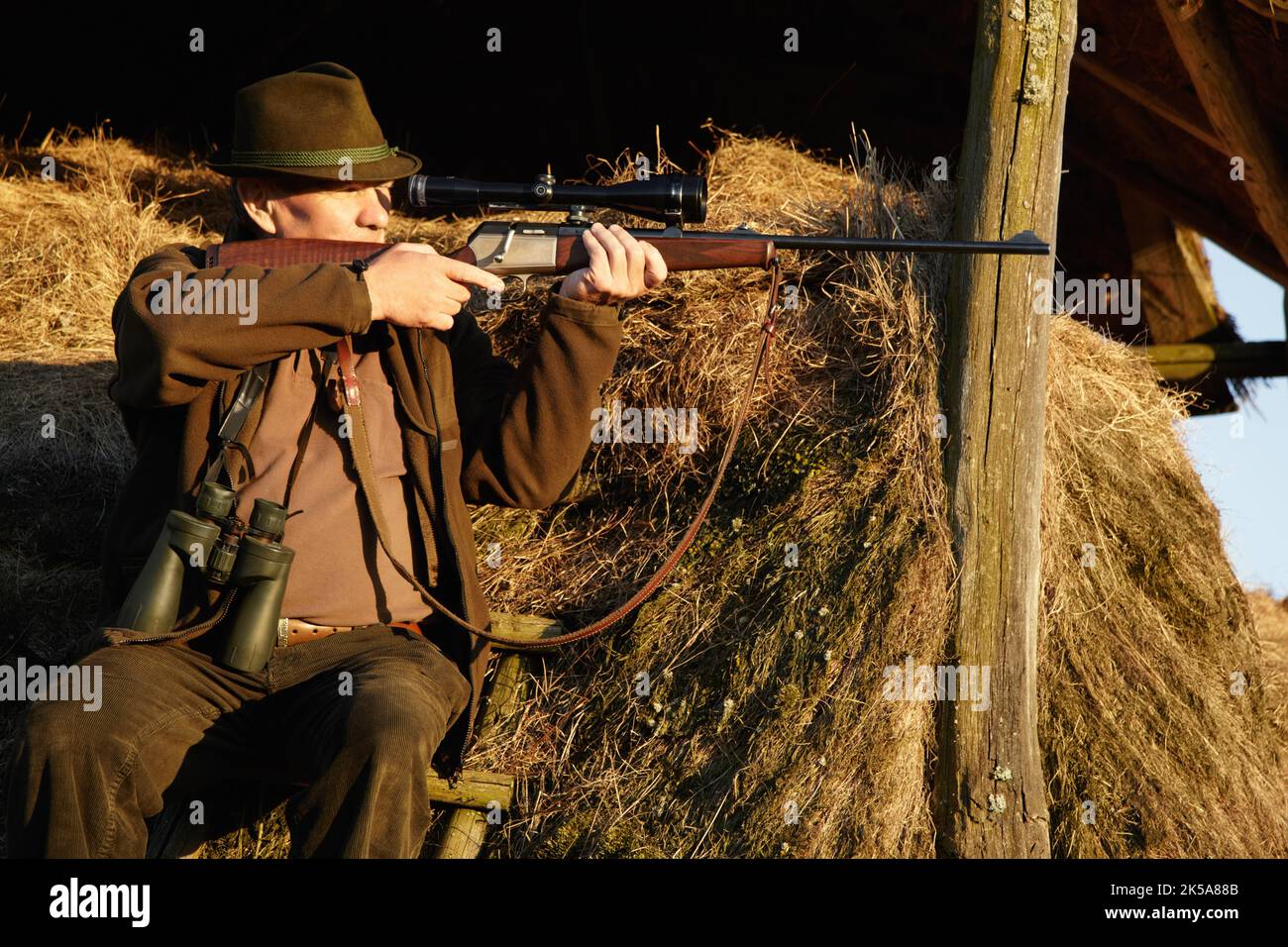 Ziel ist der Schlüssel. Ein Mann in Tarnung sitzt und mit seinem Gewehr auf etwas in einer Wildtierumgebung zielt. Stockfoto