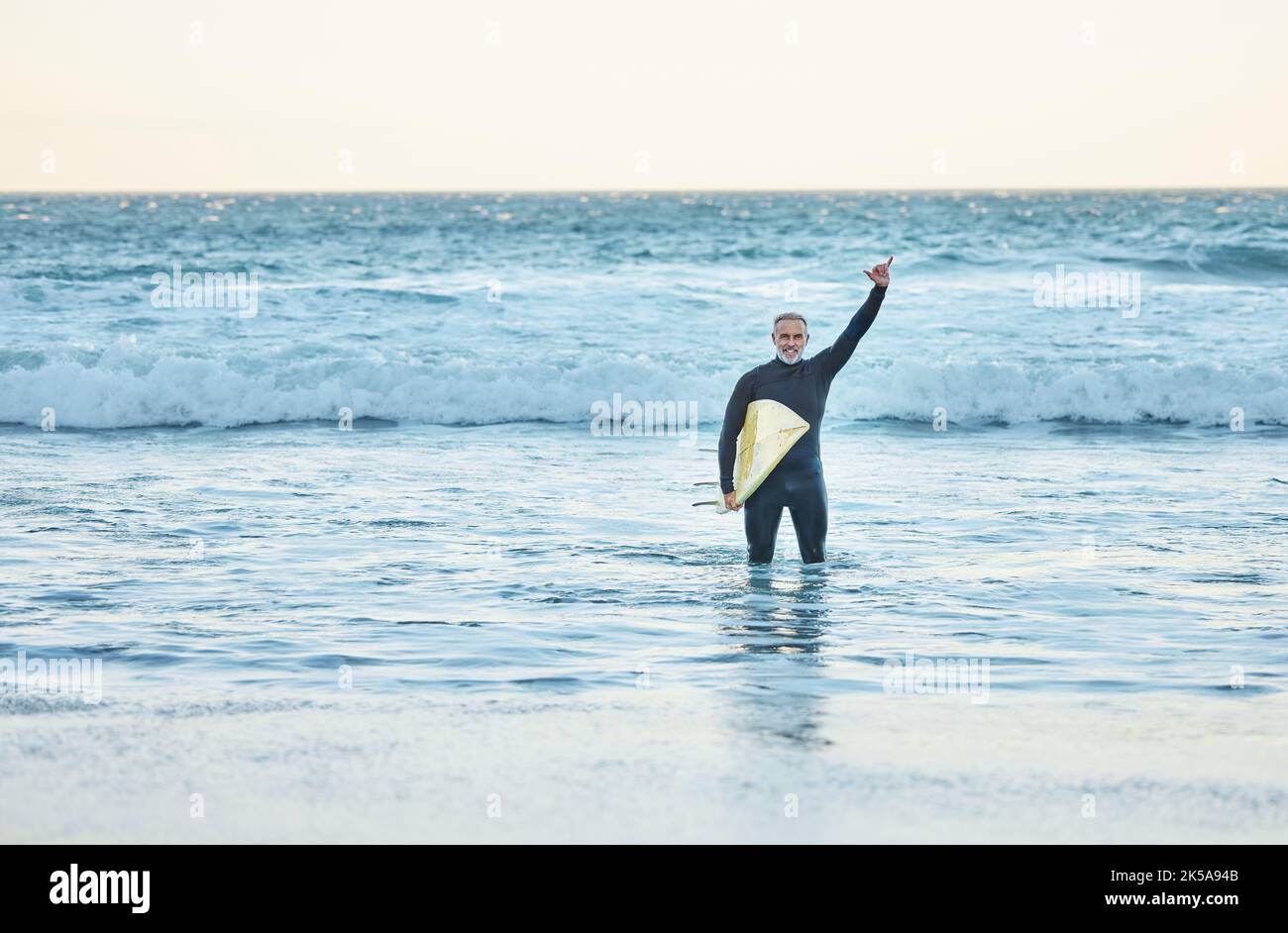 Shaka, Surfen und Sport mit einem reifen Mann, der im Sommer eine Handbewegung im Strandwasser macht. Surfer, Meer und Natur mit einem männlichen Athleten in der Stockfoto