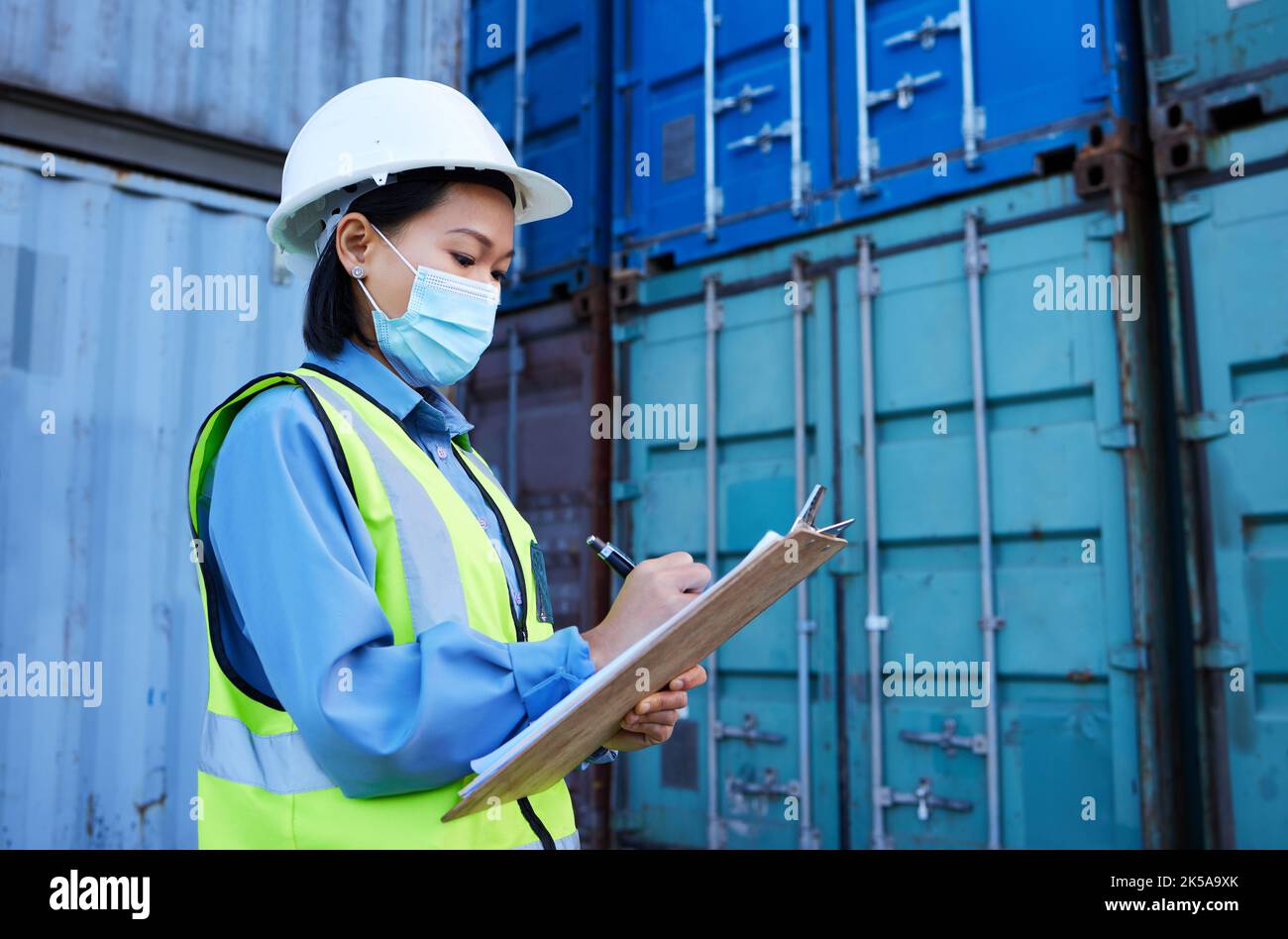 Covid, Versandlogistik und Mitarbeiter schreiben während der Inspektion in einem Containerlager. Asiatische Wirtschaftsingenieurin Frau mit E-Commerce-Notizen und Stockfoto
