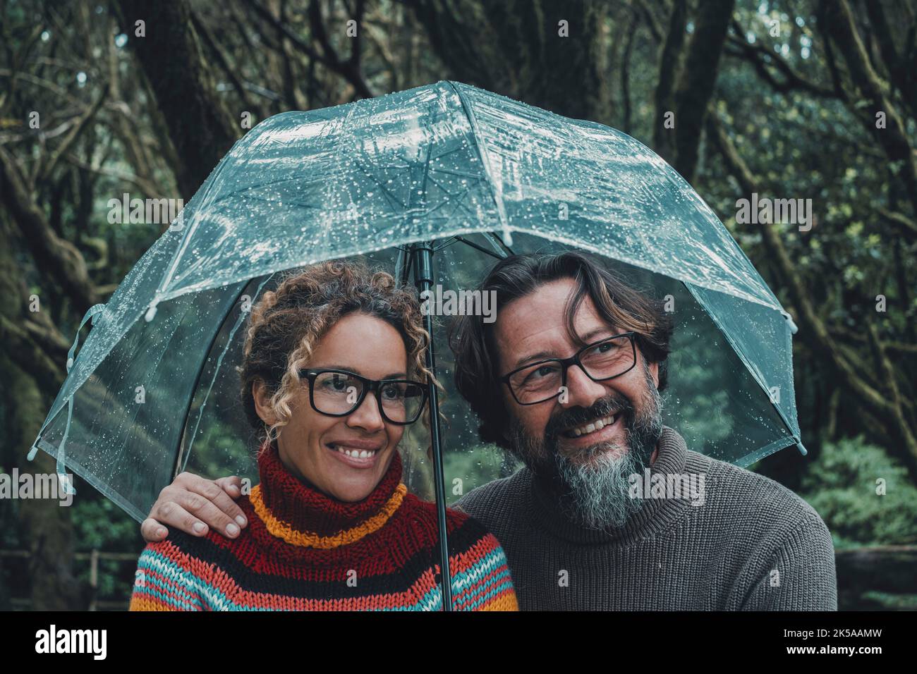 Beziehung und Liebe Paar unter dem Regen lächelnd und genießen Outdoor-Freizeitaktivitäten an regnerischen Tagen geschützt unter einem transparenten Regenschirm. Mann und Stockfoto