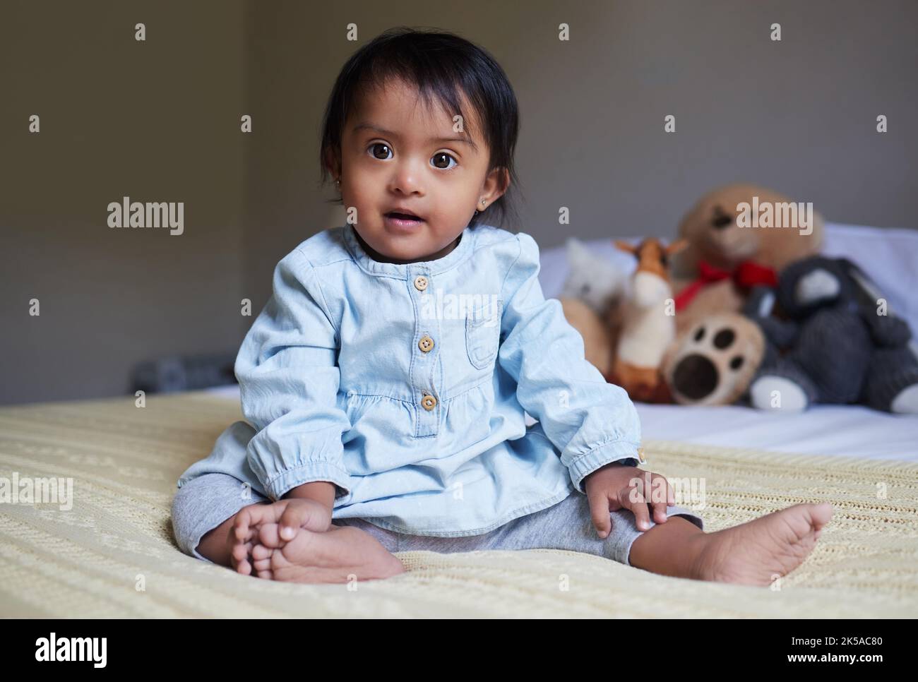 Baby, niedlich und unschuldig mit einem Mädchen auf einem Bett in ihrem Haus allein mit einem Teddybär und Stoffspielzeug im Hintergrund. Kinder, klein und rein mit einem Stockfoto