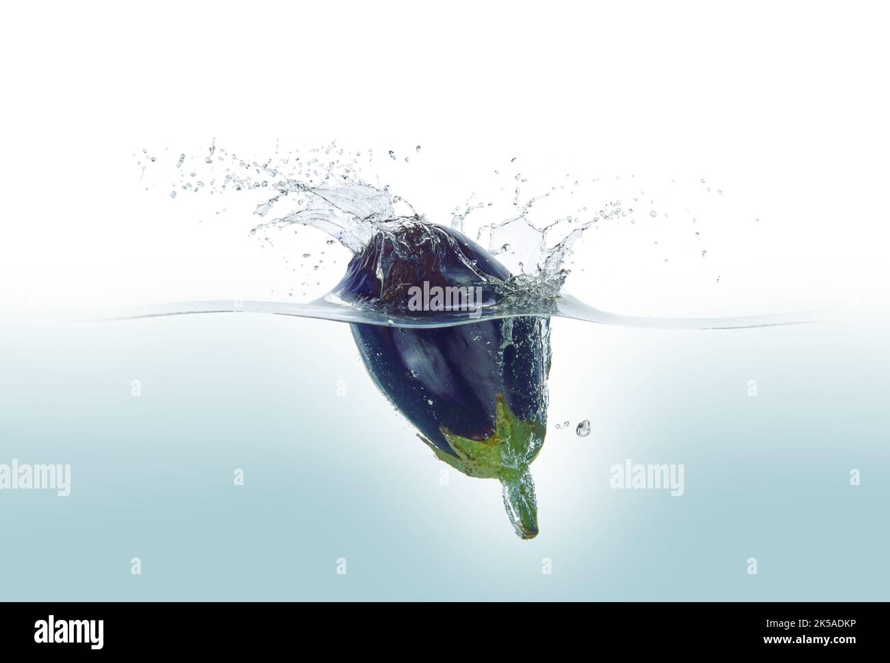 Aubergine, die in Wasser spritzt. Seitenansicht, auf weißem Hintergrund. Stockfoto