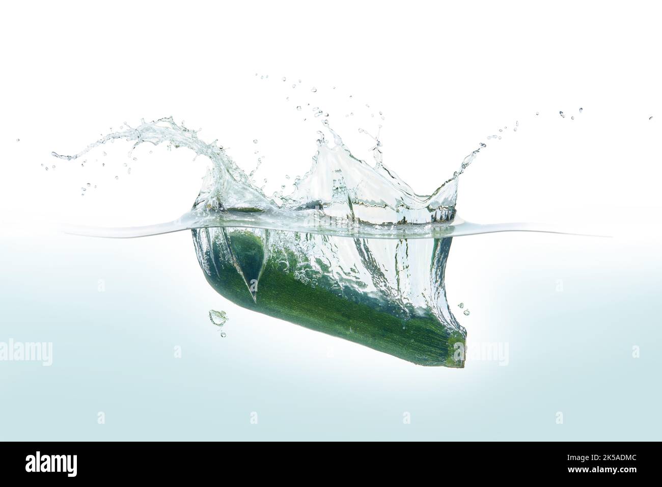 Zuchini spritzt in Wasser. Seitenansicht auf weißem Hintergrund. Stockfoto