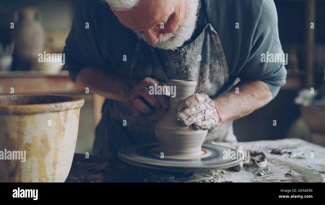 Nahaufnahme eines halbfertigen Keramikglases, das sich auf dem Töpferrad dreht und männliche Hände mit professionellen Werkzeugen Ton Formen. Erstellung von Eathenware und traditionellen Töpferei-Konzept. Stockfoto