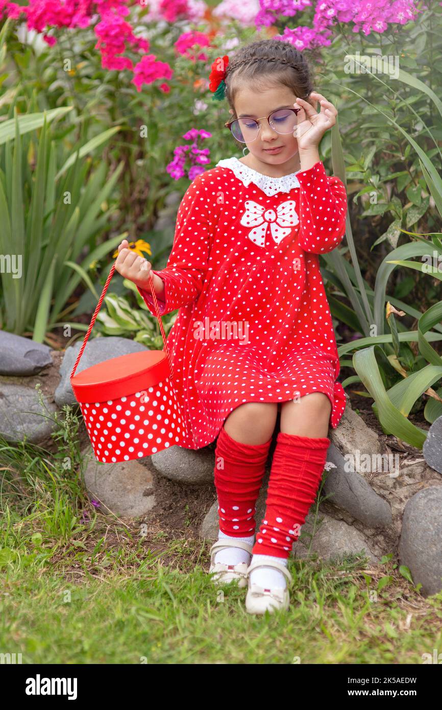 Ein kleines Mädchen in einem roten Kleid mit Polka in einer Brille Stockfoto