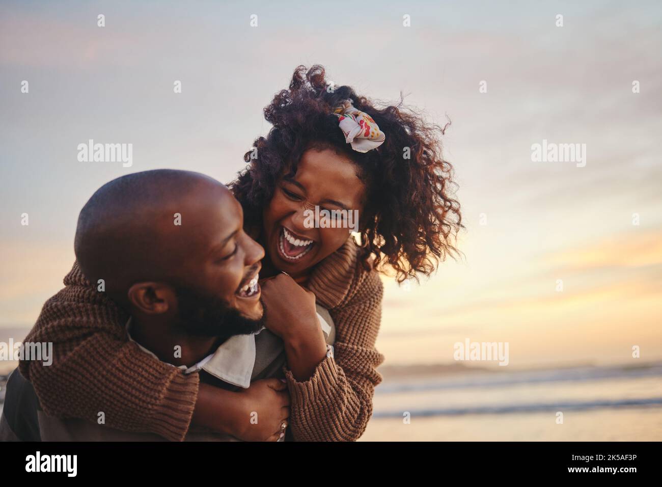 Liebe, Reise und Spaß Paar am Strand genießen Sommerurlaub oder Flitterwochen bei Sonnenuntergang mit einem Piggy Rücken reiten, während sie spielerisch. Lachen, Energie und Stockfoto