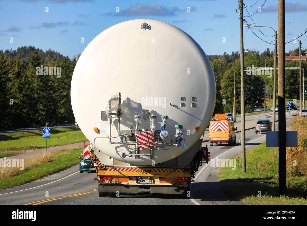 Rückansicht des Überlasttransports eines LNG-Lagersilos im Straßenverkehr, unterstützt durch ein Pilotfahrzeug. Salo, Finnland. 22. September 2022. Stockfoto