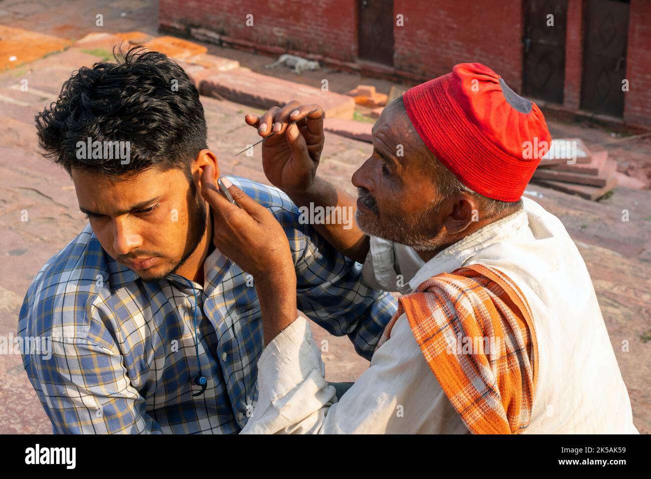 NEU-DELHI - SEP 17: Indischer Straßenarbeiter mit einer Nadel, die am 17. September in einer Straße in Neu-Delhi das Ohr einer Person reinigt. 2022 in Indien. Stockfoto
