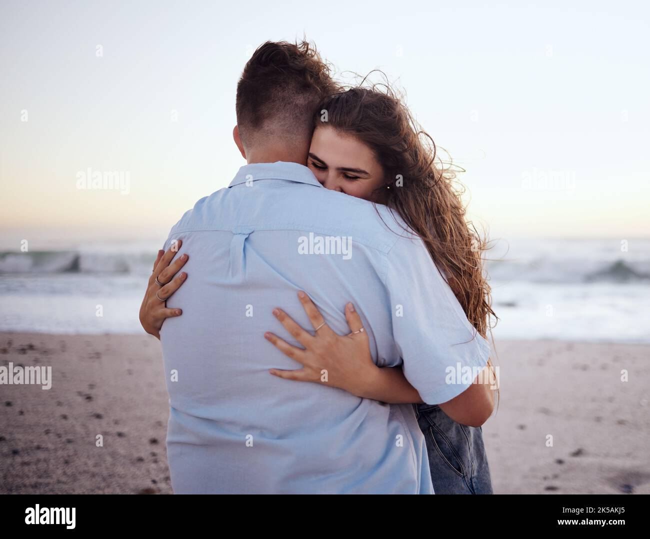 Liebe, Umarmung und Romantik mit einem Paar am Strand bei einem Date im Sand am Meer oder am Meer bei Sonnenuntergang. Sommer, Natur und Reisen mit einem jungen Mann Stockfoto