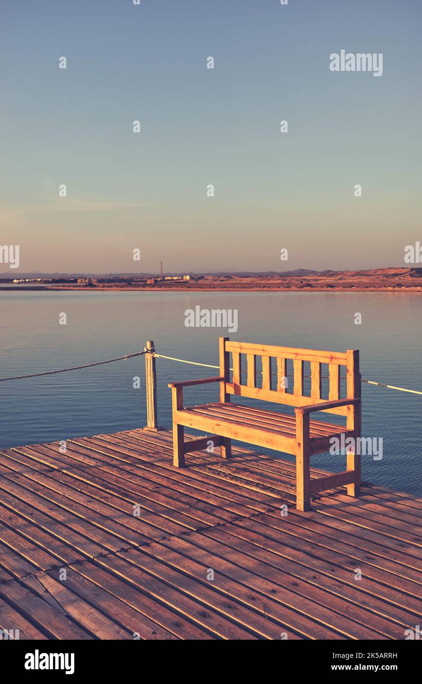 Eine leere Bank auf einem hölzernen Pier bei Sonnenuntergang, Farbtonierung aufgetragen. Stockfoto
