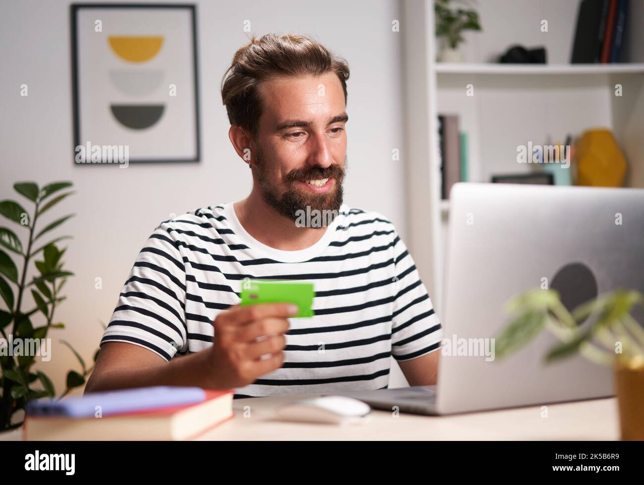 Fröhlicher junger Mann, der zu Hause E-Shopping macht. Glücklicher kaukasischer Mann, der Online-Zahlungen mit Karte macht. Stockfoto