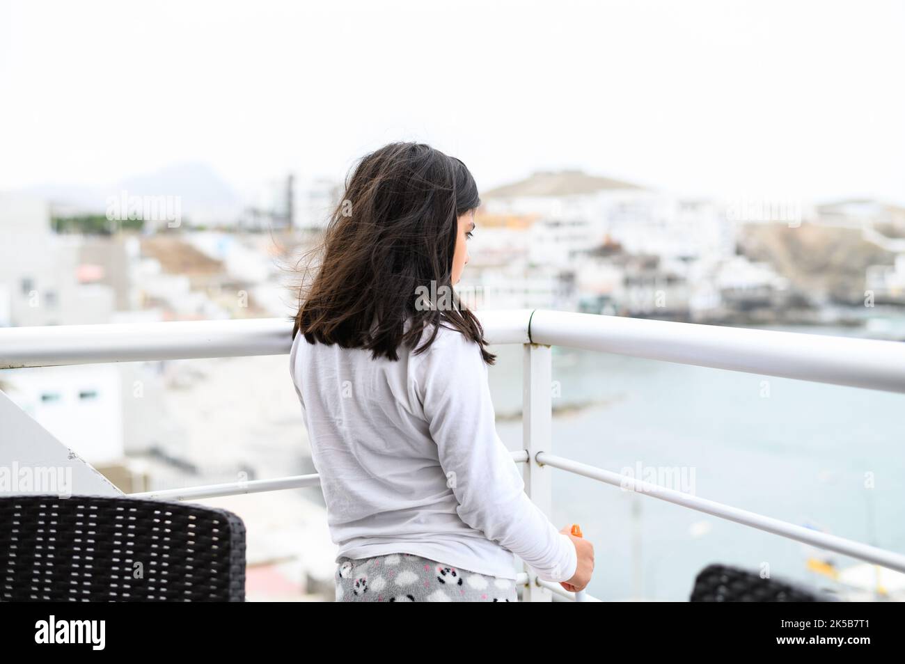 Kleines Mädchen, das auf dem Balkon mit Blick auf das Meer steht Stockfoto