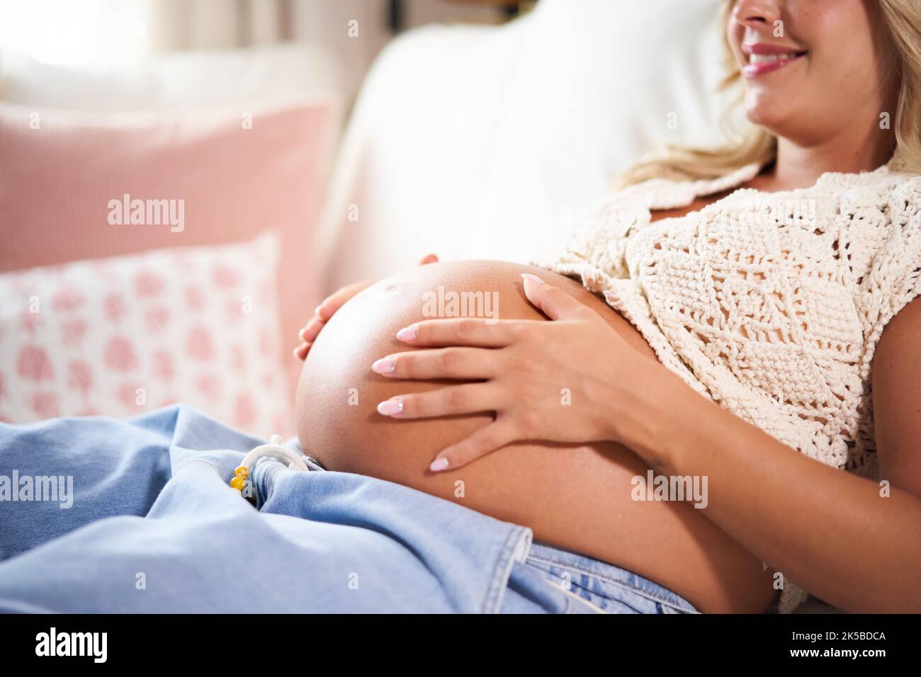 Süßes und glückliches Foto einer Schwangeren, die ihren Bauch kuschelt, während sie zu Hause auf dem Sofa liegt. Stockfoto