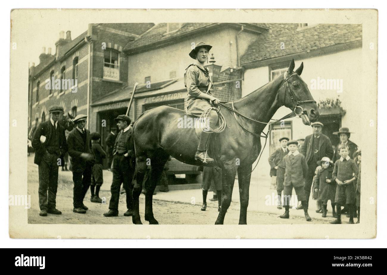 Die ursprünglich aus dem Jahr WW1 stammende Postkarte, eine Kriegsarbeiterin, ein Landmädchen, wird von einer Gruppe von Zuschauern beobachtet, die von einer Frau fasziniert ist, die Hosen und Reiten trägt, und nicht vom Seitensattel. Sie trägt ein Seil. Möglicherweise arbeitet sie mit Kavalleriepferden. Sie trägt eine Schärpe mit einem Blumenknopfloch. Möglicherweise nimmt sie an einer Art Parade Teil. Möglicherweise Schottland, wie Barry, Dundee auf der Rückseite schrieb. Stockfoto