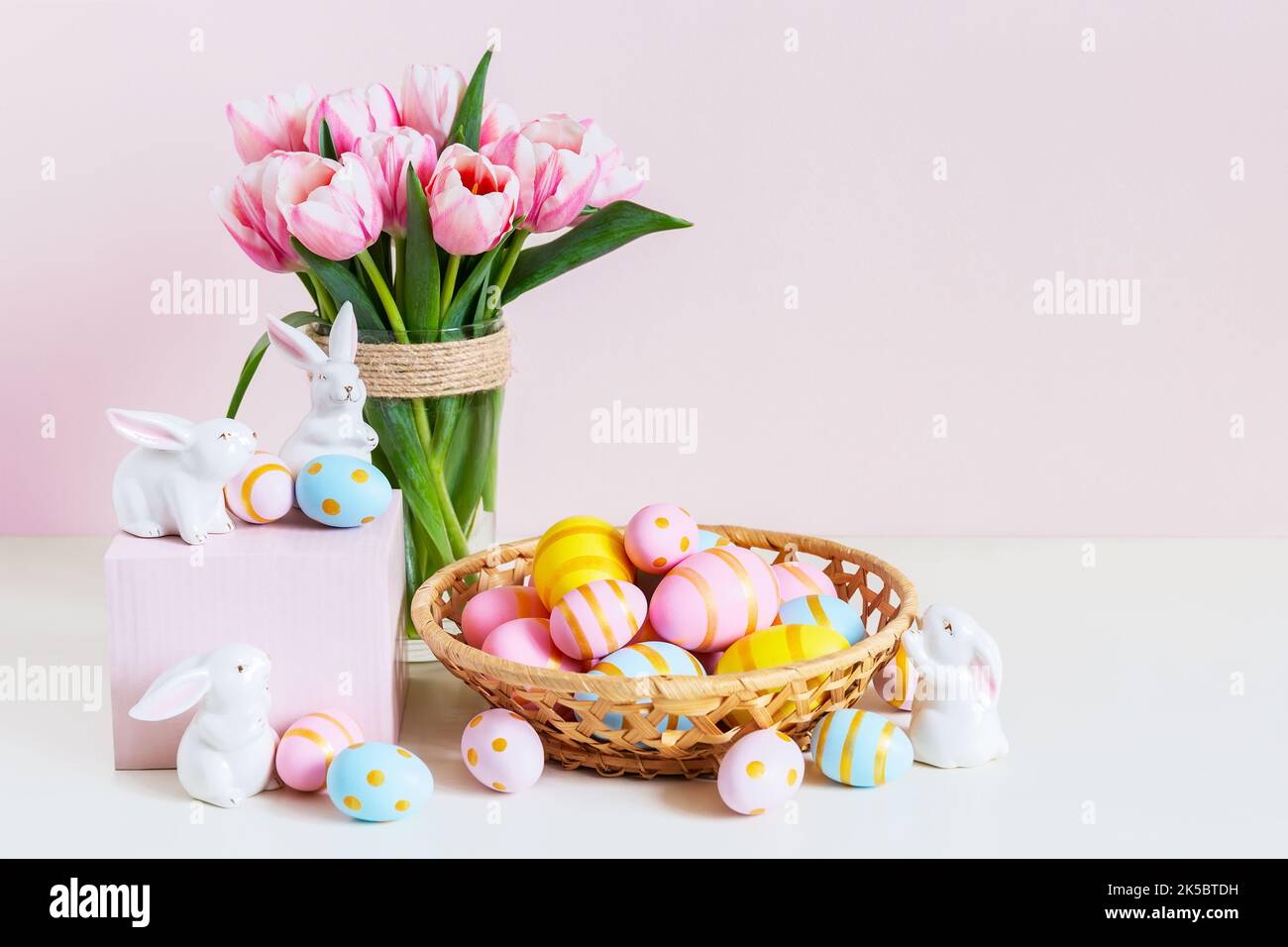 Ostern und Frühlingsferien Grußkartenkonzept. Rosa Tulpen, osterhasen mit bunten Eiern im Korb. Bemalte Ostereier im Nest und Tulpen mit Stockfoto