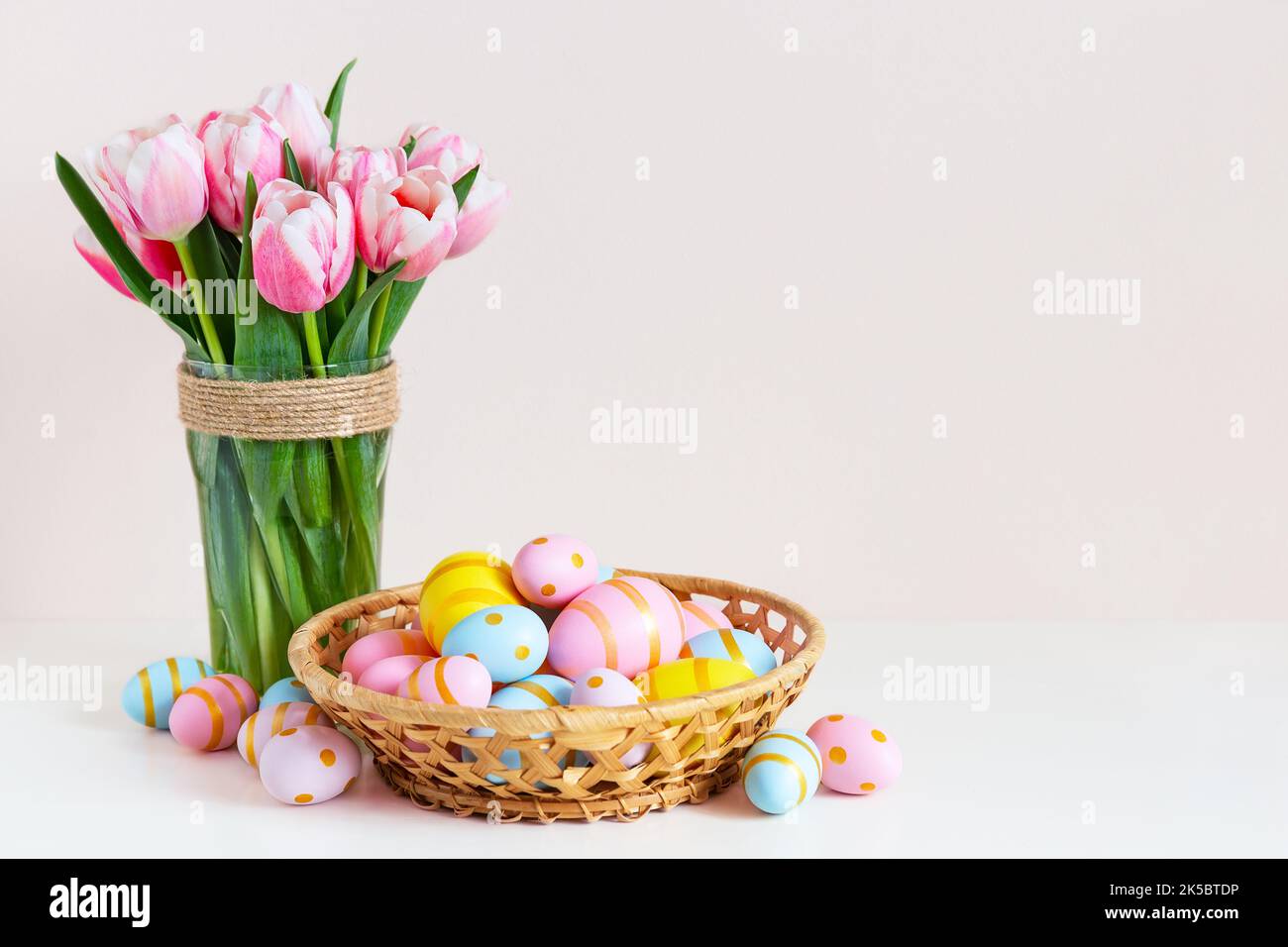 Ostern und Frühlingsferien Grußkartenkonzept. Rosa Tulpen mit bunten Eiern im Korb. Bemalte Ostereier im Nest und Tulpen auf farbigem Hintergrund Stockfoto