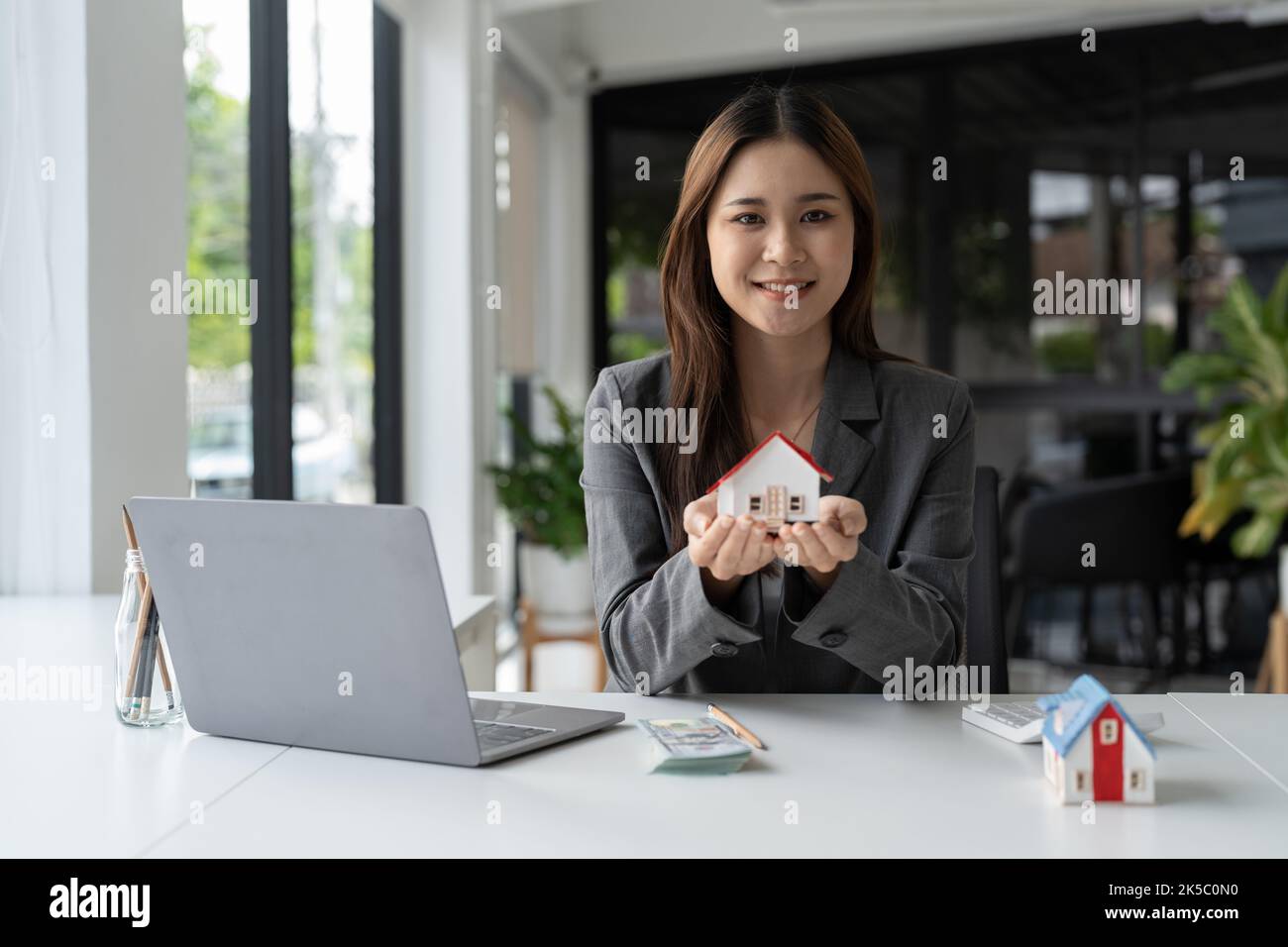 Porträt der schönen jungen Immobilienmakler Geschäftsfrau hält Hausschlüssel und Haus Mockup Stockfoto