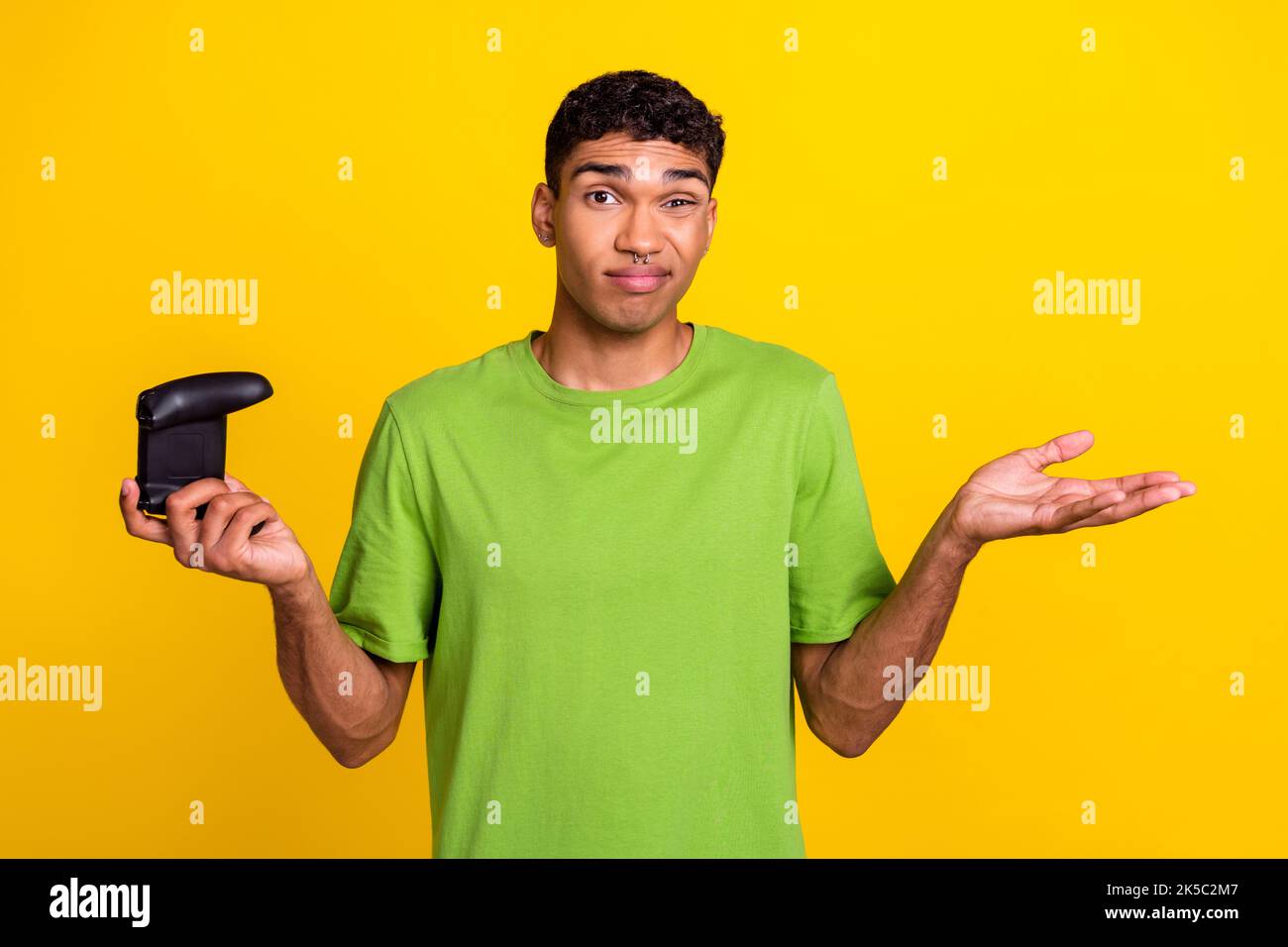 Foto von jungen gut aussehenden lustigen Kerl Grimace weiß nicht, keine Idee halten drahtlose Joystick Spieler Handflächen Problem tut mir leid isoliert auf gelbem Hintergrund Stockfoto