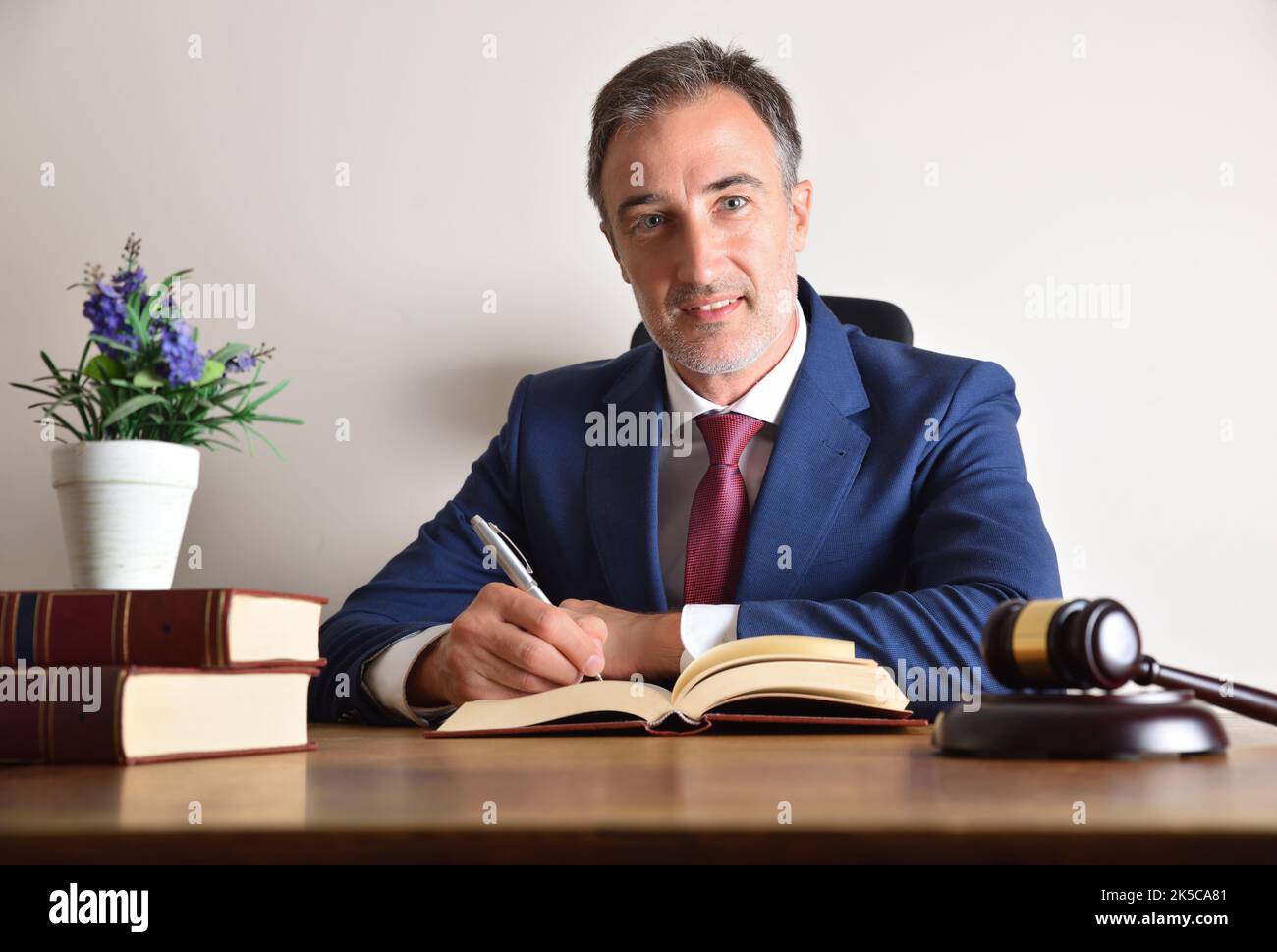 Gut geeigneter Anwalt, der auf seinem Bürotisch mit Büchern und Richtergavel und isoliertem weißen Wandhintergrund unterschrieb. Vorderansicht. Stockfoto