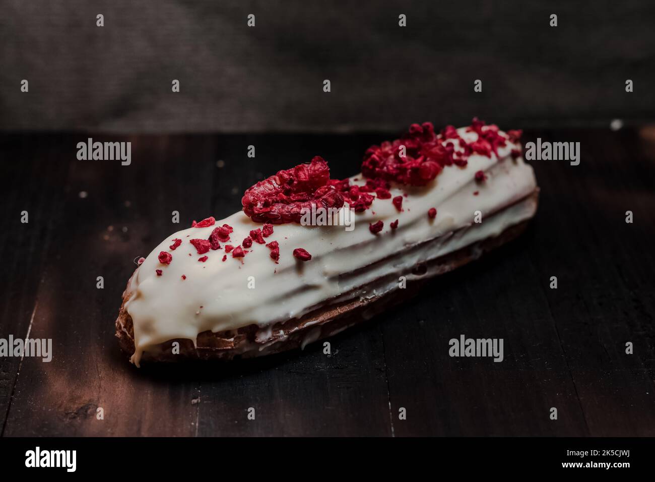 Nahaufnahme eines traditionellen französischen Dessertes eclair mit weißer Schokolade und Himbeeren auf dunklem Hintergrund Stockfoto