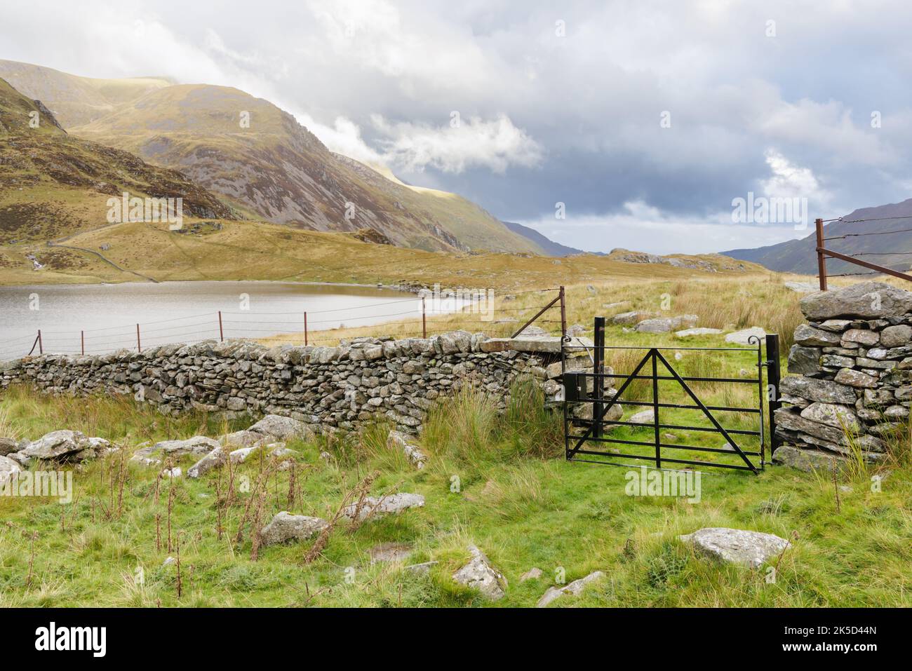 Wales, Großbritannien, 2022. September: Ein Metalltor in einer Trockensteinmauer in der Nähe des Ufers von Lynn Idwal mit Pinnacle Crag und dann Y Llymllwyd in der Ferne. Stockfoto