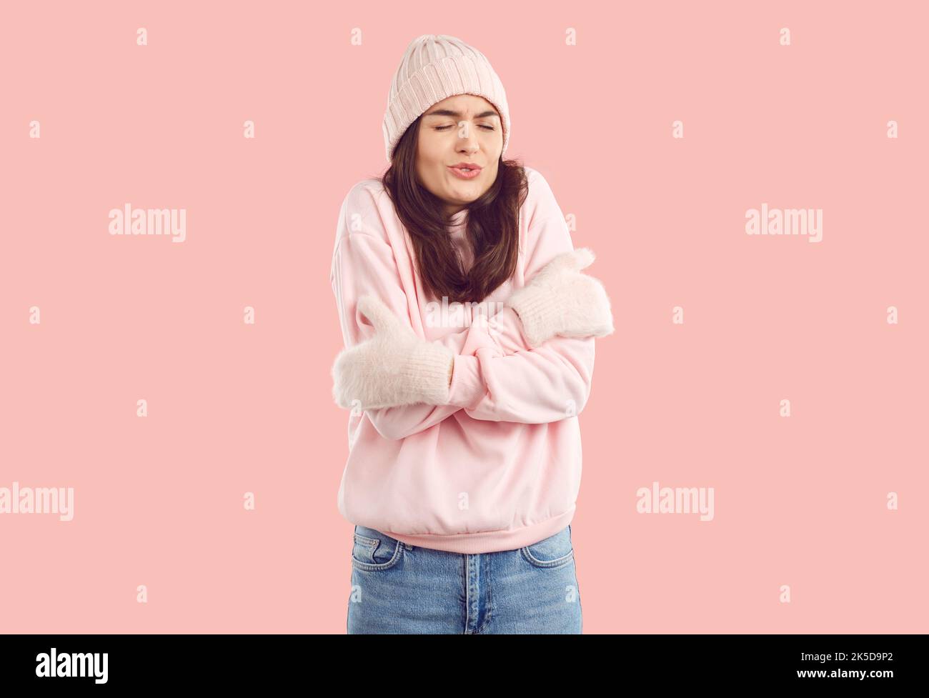 Junge Frau in warmen rosa Winterkleidung fühlt sich kalt, eiskalt und zitternd an Stockfoto