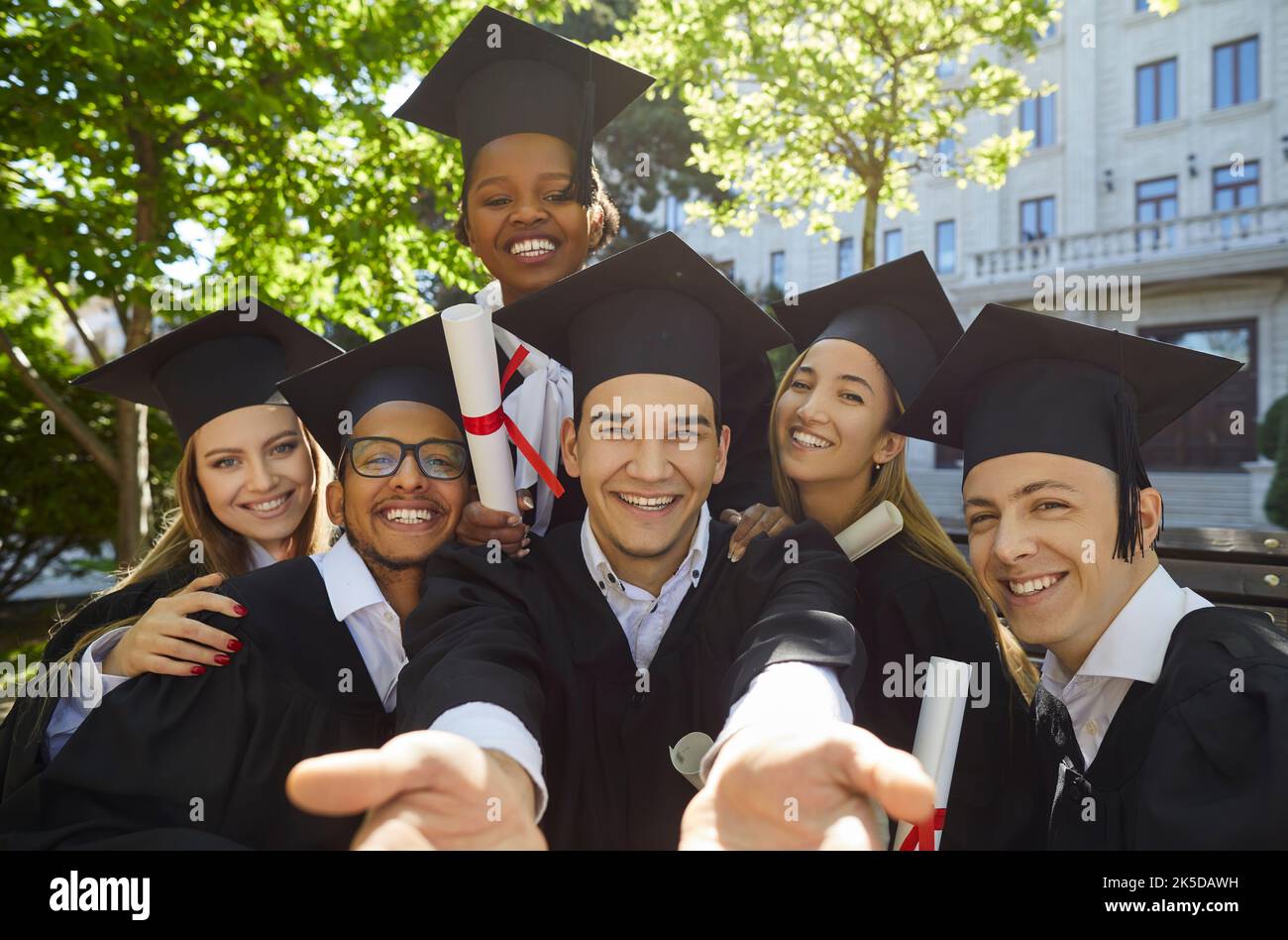 Aufgeregt multikulturelle Menschen in Abschlusskittel mit Diplomen posieren für Gruppen-Selfie-Foto. Stockfoto