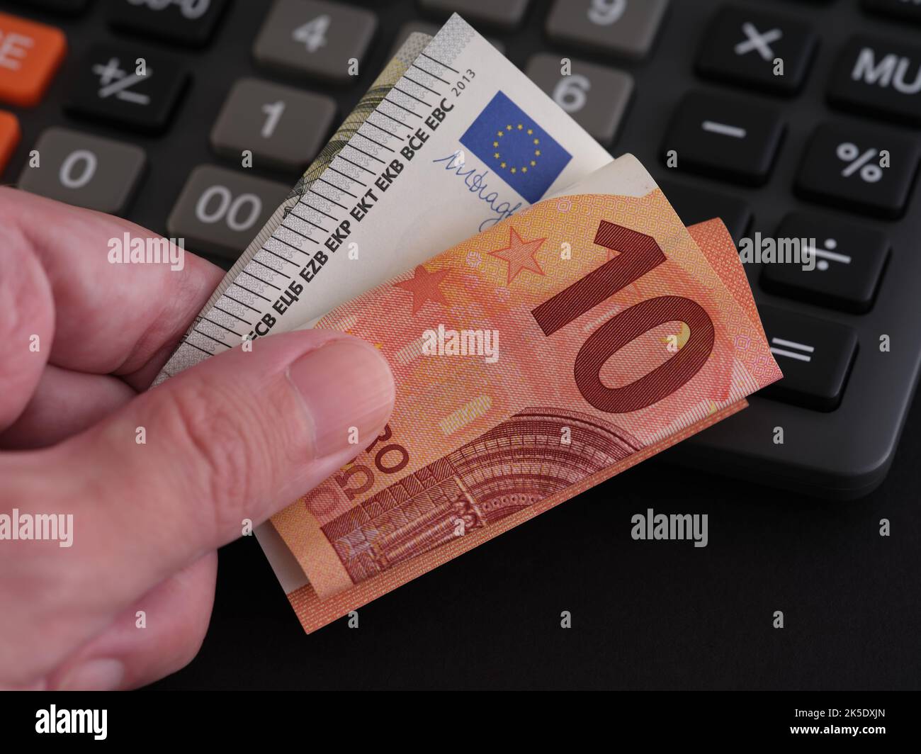 Ein Mann, der Euro-Banknoten in der Hand hält, mit einem Rechner im Hintergrund. Nahaufnahme. Stockfoto