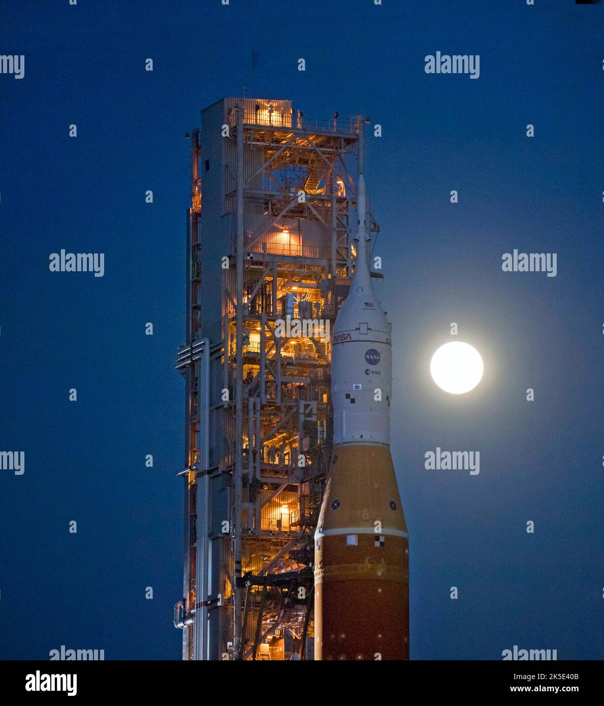 Der Mond steigt hinter der NASA-Rakete Space Launch System (SLS) mit der Orion-Sonde auf einem mobilen Trägerrakete auf, während er zum ersten Mal am 17. März 2022 im Kennedy Space Center der NASA in Florida, USA, zum Launch Complex 39B ausrollt. Im Vorfeld des Artemis I-Flugtests der NASA werden die vollständig gestapelte und integrierte SLS-Rakete und die Orion-Raumsonde im Launch Complex 39B einer Nassprobe unterzogen, um die Systeme zu verifizieren und Countdown-Verfahren für den ersten Start zu üben. Eine optimierte Version eines Originalbildes der NASA. Quelle: NASA/Agemignani Stockfoto