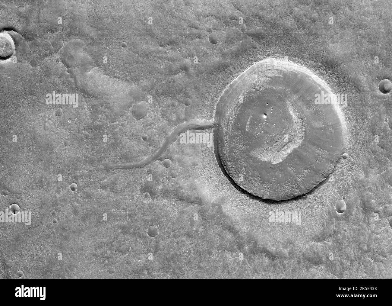 Dieses Bild vom Mars Reconnaissance Orbiter (MRO) der NASA zeigt einen Einschlagskrater, der aufgrund des Tals, das von Wasser geformt wurde, das es früher füllte, amüsant wie ein Kaulquappe aussieht. Es ist oft schwierig, zwischen ein- und Auslasskanälen zu unterscheiden, aber das Wasser fließt immer bergab. In diesem speziellen Fall können wir daraus schließen, dass Wasser nach außen fließt, weil wir über die erforderlichen Geländehöheninformationen verfügen. Eine optimierte und verbesserte Version von NASA-Bildern. Quelle: NASA/JPL/UArizona Stockfoto
