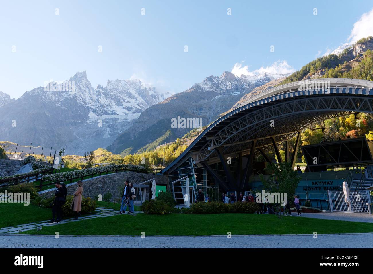 Seilbahnstation am unteren Ende des Skyway Monte Bianco Seilbahnsystems, Aosta Valley Italien. Die Touristen warten auf dem Grund mit Bergen dahinter. Stockfoto