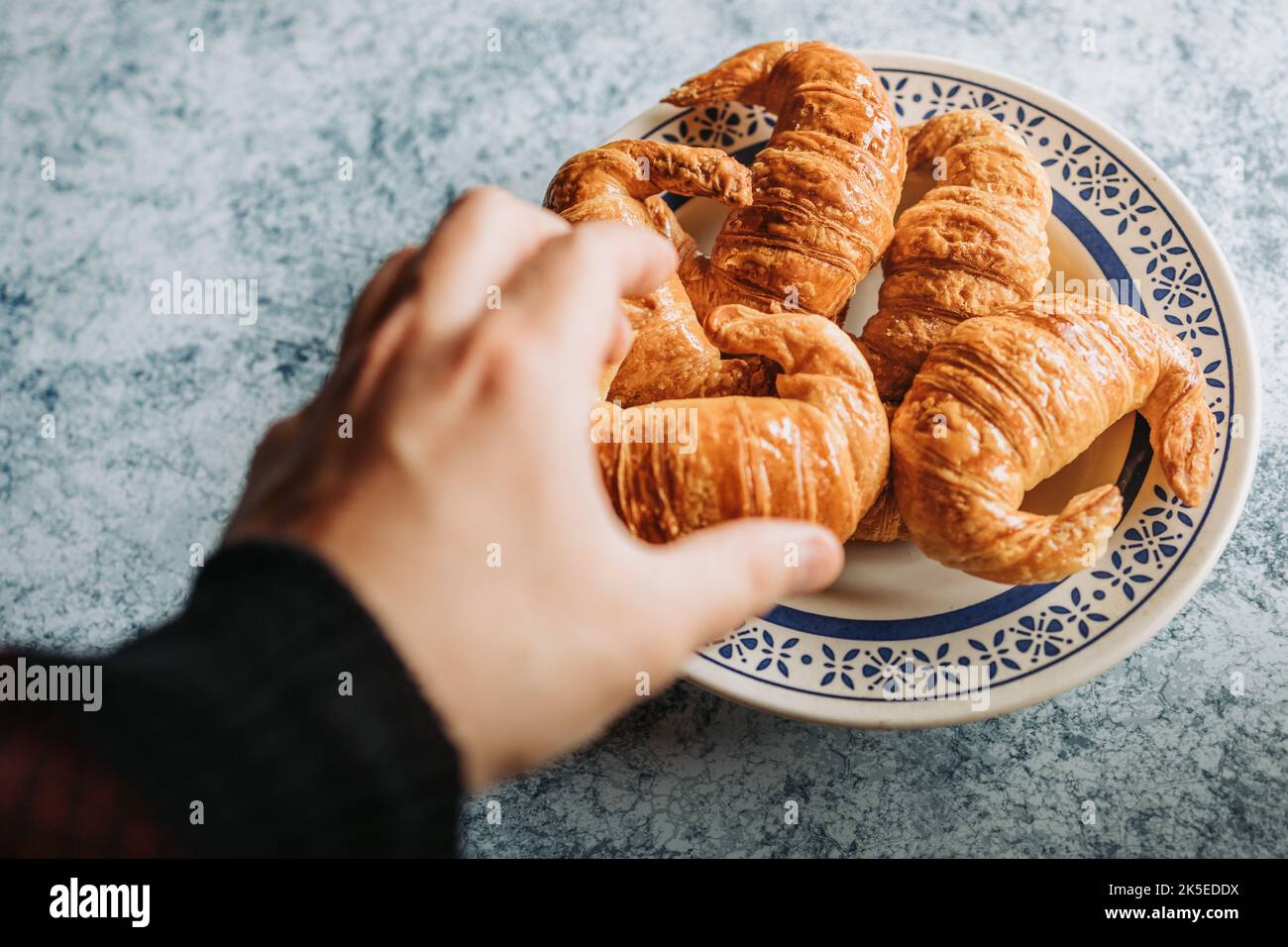 Die Hand des Mannes erreicht einen Teller mit Medialunas, einem süßen argentinischen Croissant. Stockfoto