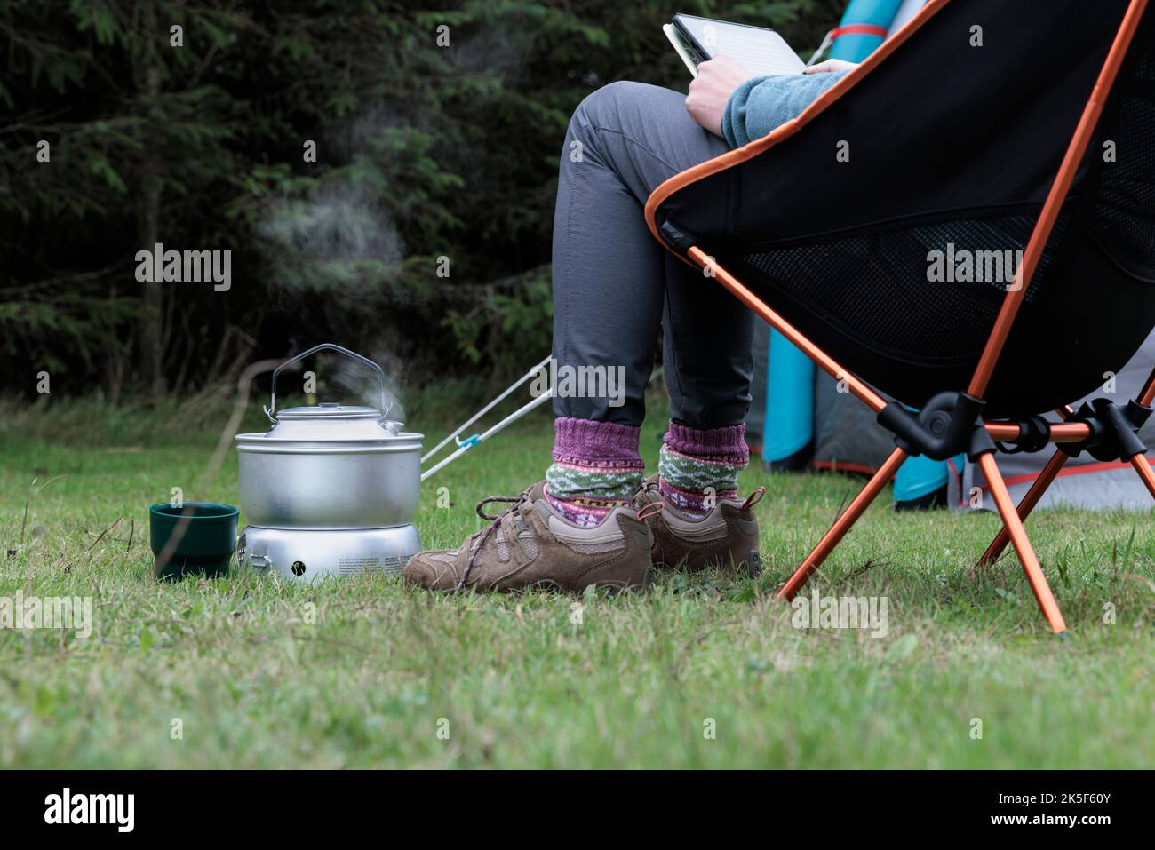 Frau liest und kocht einen Wasserkocher auf einem Campingkocher. Stockfoto