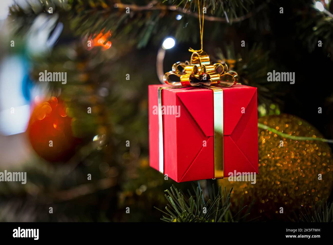 Große rote Farbe Box Überraschung Gelb Band Schleife Bokeh Hintergrund. Geschenk für Urlaub im Winter Dezember. Grüner Astbaum mit Kugeldeko. Frohes Ne Stockfoto