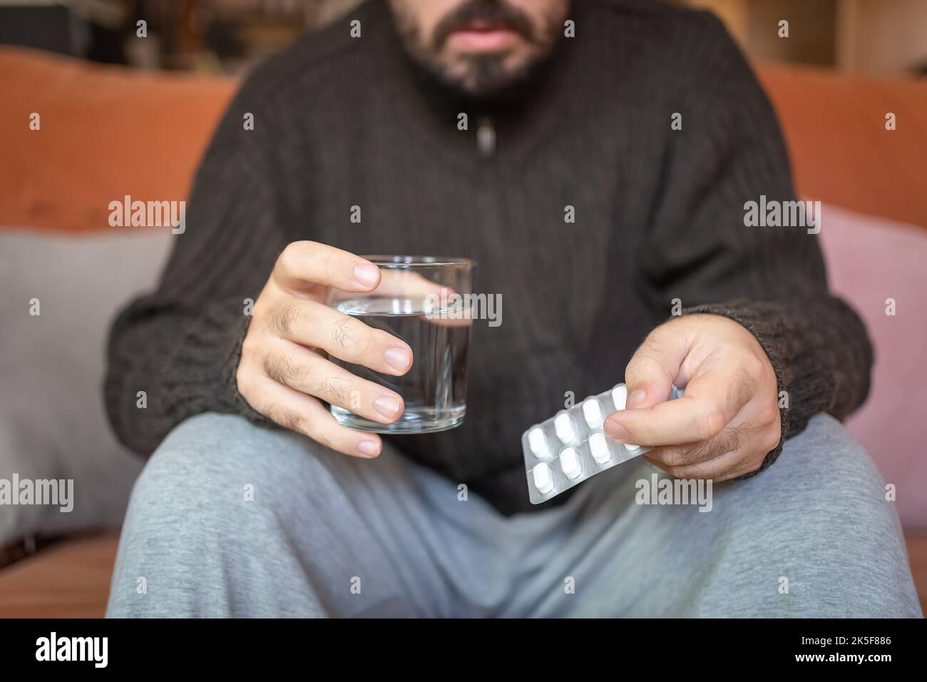 Kranker Mann mit einer Packung Pillen und einem Glas Wasser zum Trinken. Stockfoto