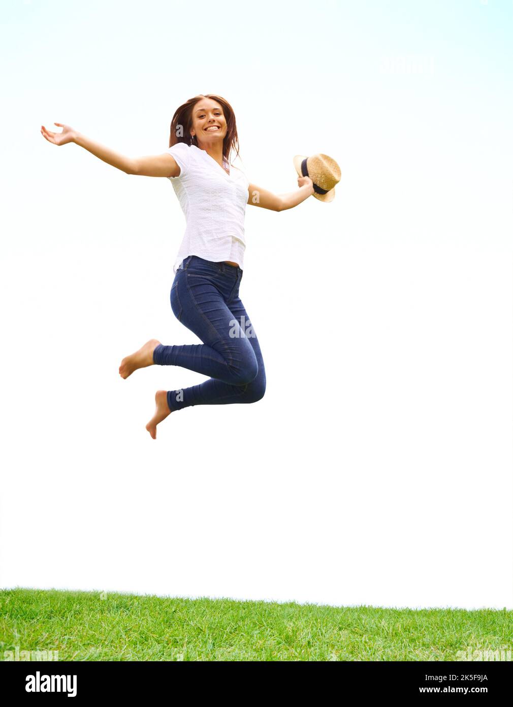 Gefüllt mit den Freuden des Frühlings. Junge Frau springt vor Freude, während sie sich an ihrem Hut festhält. Stockfoto