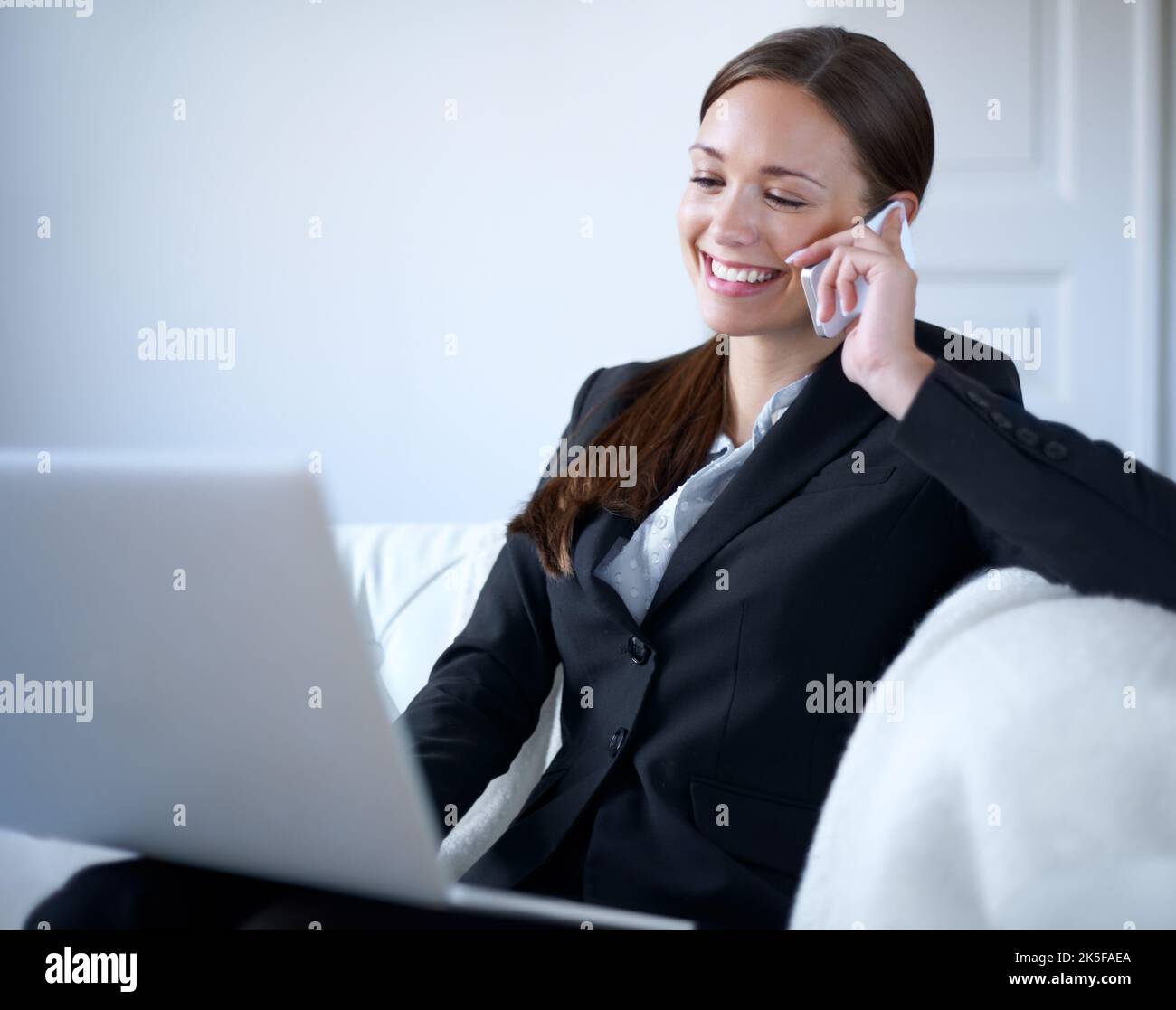 Es ist toll, von Ihnen zu hören ... attraktive junge Geschäftsfrau mit ihrem Laptop zu Hause, während auf ihrem Handy. Stockfoto