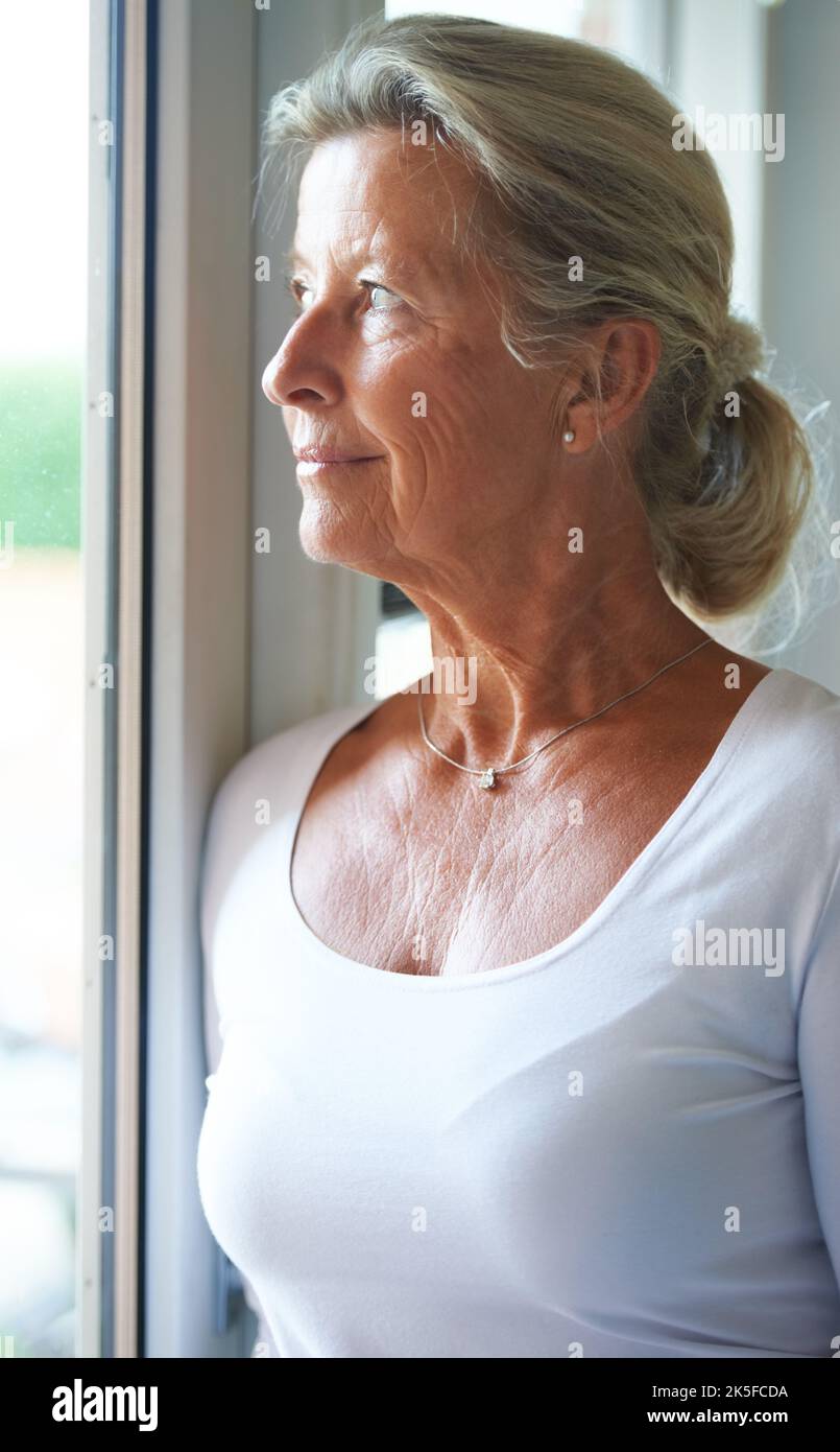 In Anbetracht ihrer Rentenoptionen. Ältere Frau schaut nachdenklich aus dem Fenster. Stockfoto