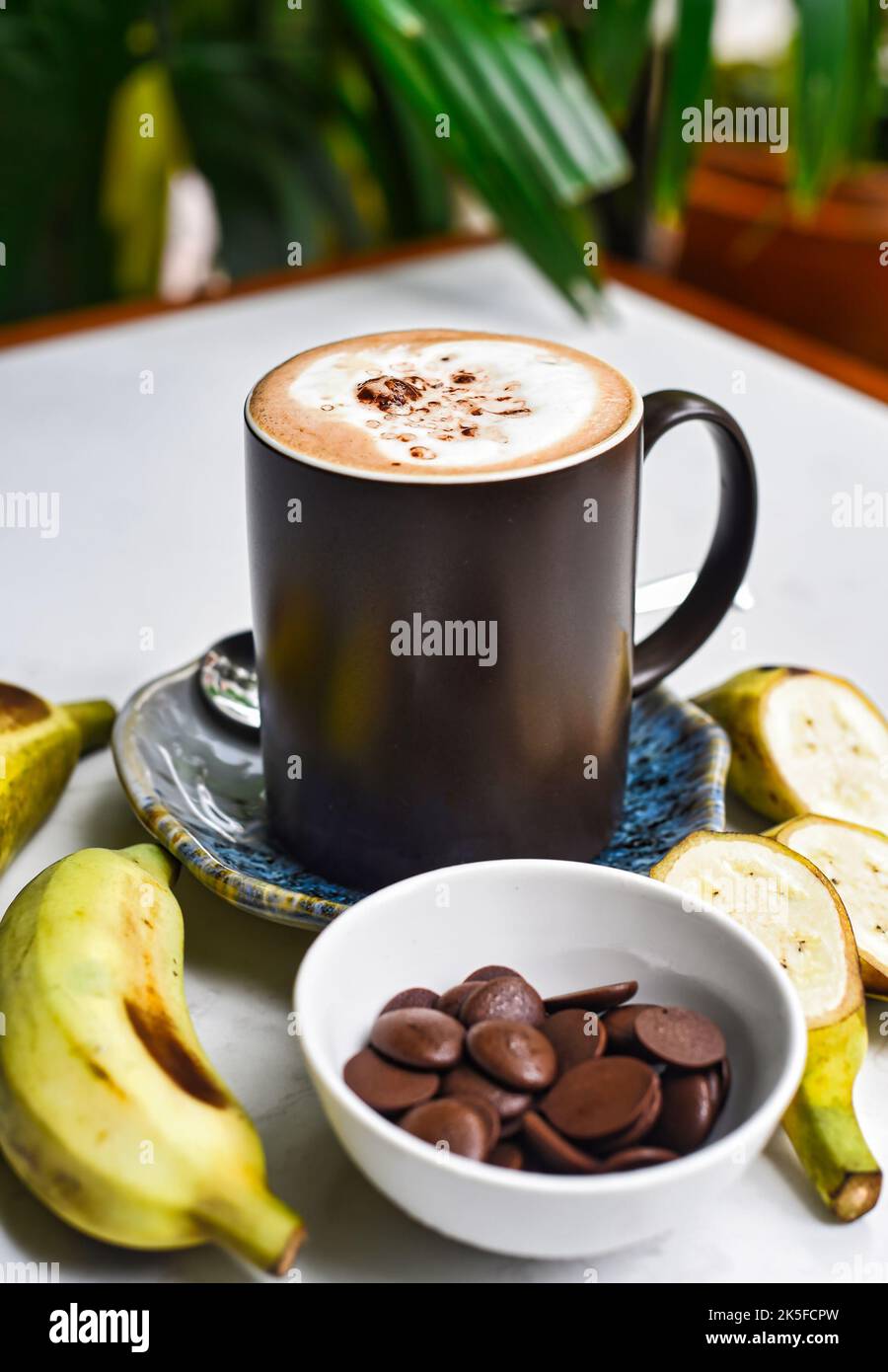 Bananenschokolade-Latte mit frischen Bananen- und Schokoladentropfen auf weißem Tisch Stockfoto