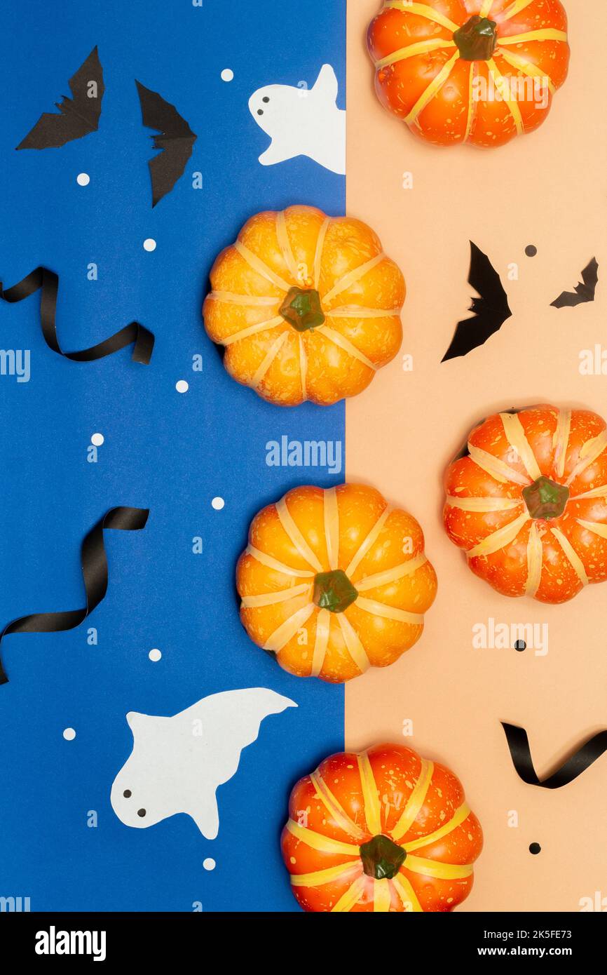 Halloween-Konzept, gruselige Kürbisse mit Geist und schwarzer Fledermaus auf blauem und cremefarbenem Hintergrund. Stockfoto