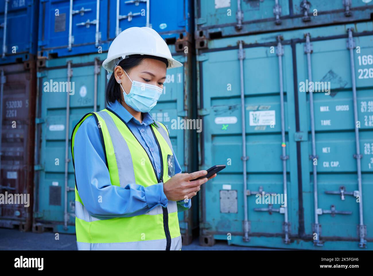 Covid, Mitarbeiter in sozialen Medien und Logistik, liest Chat am Telefon und arbeitet in einer Containerfabrik. Asiatischer Industriemitarbeiter mit Gesichtsmaske im Web für Stockfoto