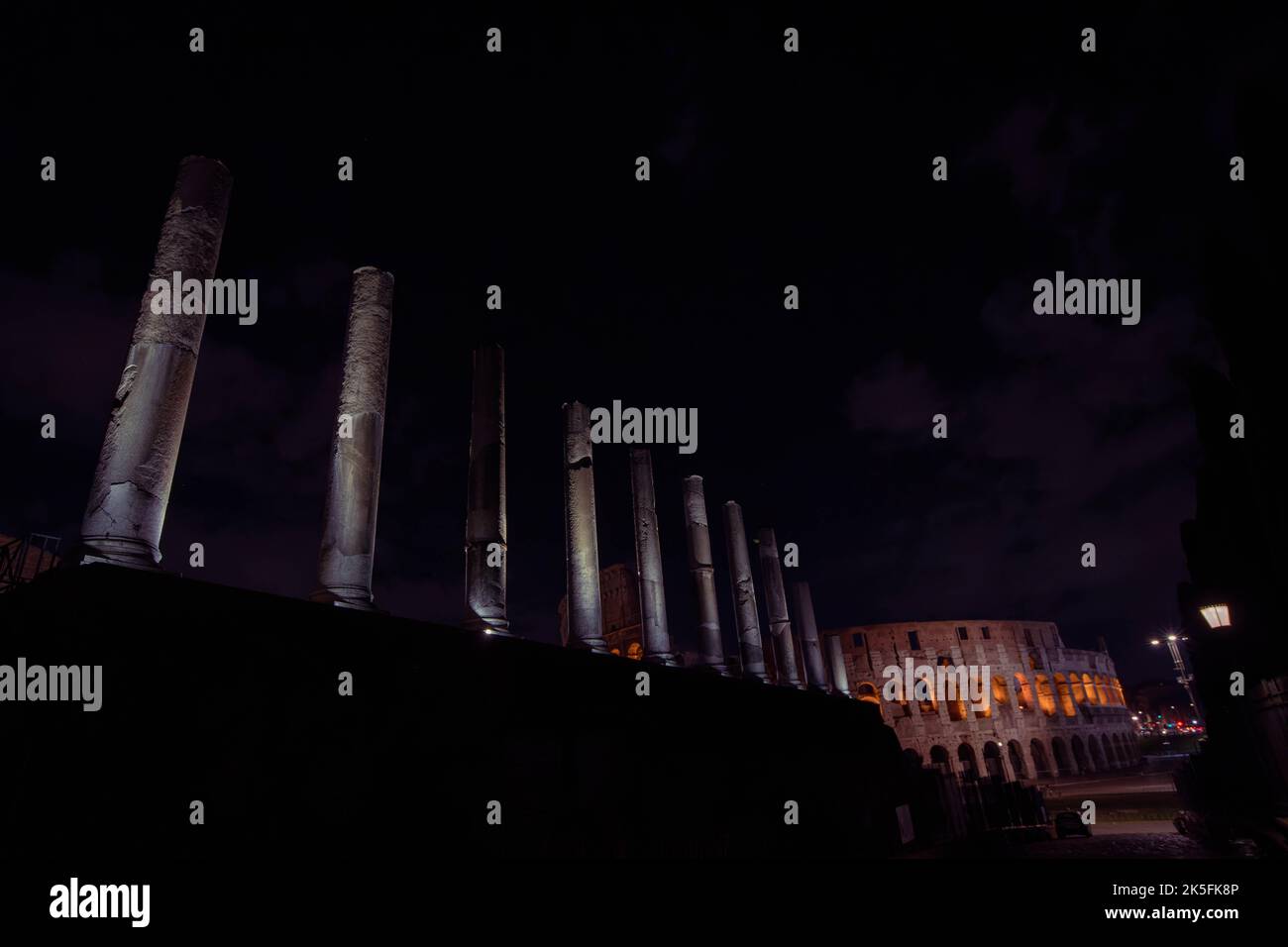 Antike römische Säulen, beleuchtet bei Nacht mit Kolosseum im Hintergrund Stockfoto