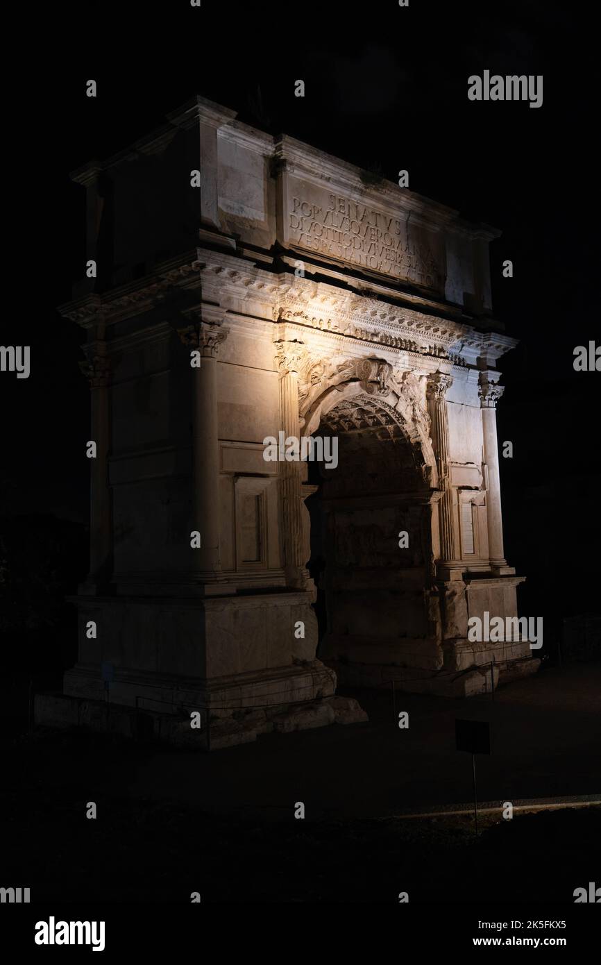 Der antike römische Bogen beleuchtet bei Nacht mit klassischen Säulen und lateinischer Inschrift Stockfoto