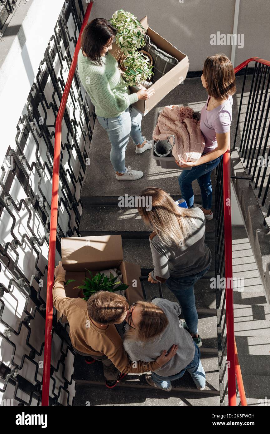 Vertikaler Vorgeschmack auf die Erwartung, dass Studentenfreunde sich küssen, Sachen auf Treppen tragen, während man den Umzug durchmacht und den neuen Campus umzieht Stockfoto