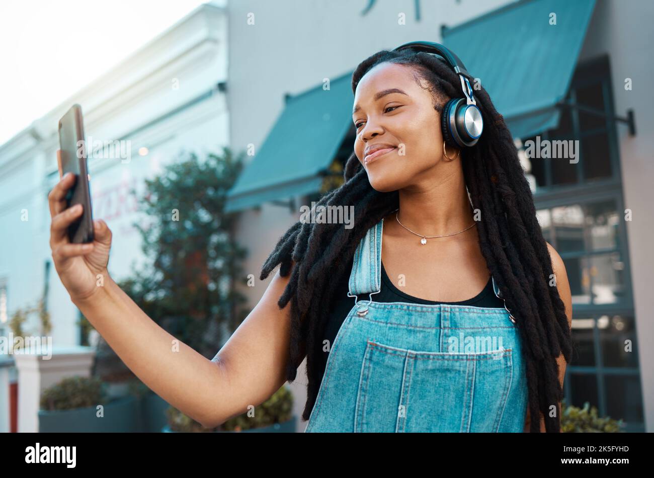 Telefon, Selfie und glückliche schwarze Frau auf der Straße der Stadt mit Kopfhörern, die Musik, Podcast oder Radio hören. Glück, Technologie und afrikanisches Mädchen auf Stockfoto