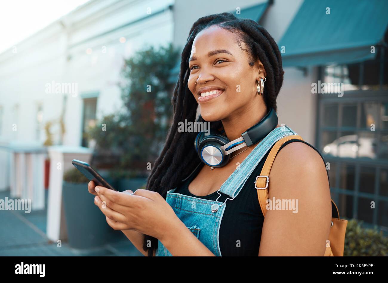 Student, Telefon und schwarze Frau auf der Straße mit Kopfhörern auf dem Weg zur Hochschule in Südafrika. Glücklich, Lächeln und schöne afrikanische Mädchen in Outdoor-Stadt Stockfoto